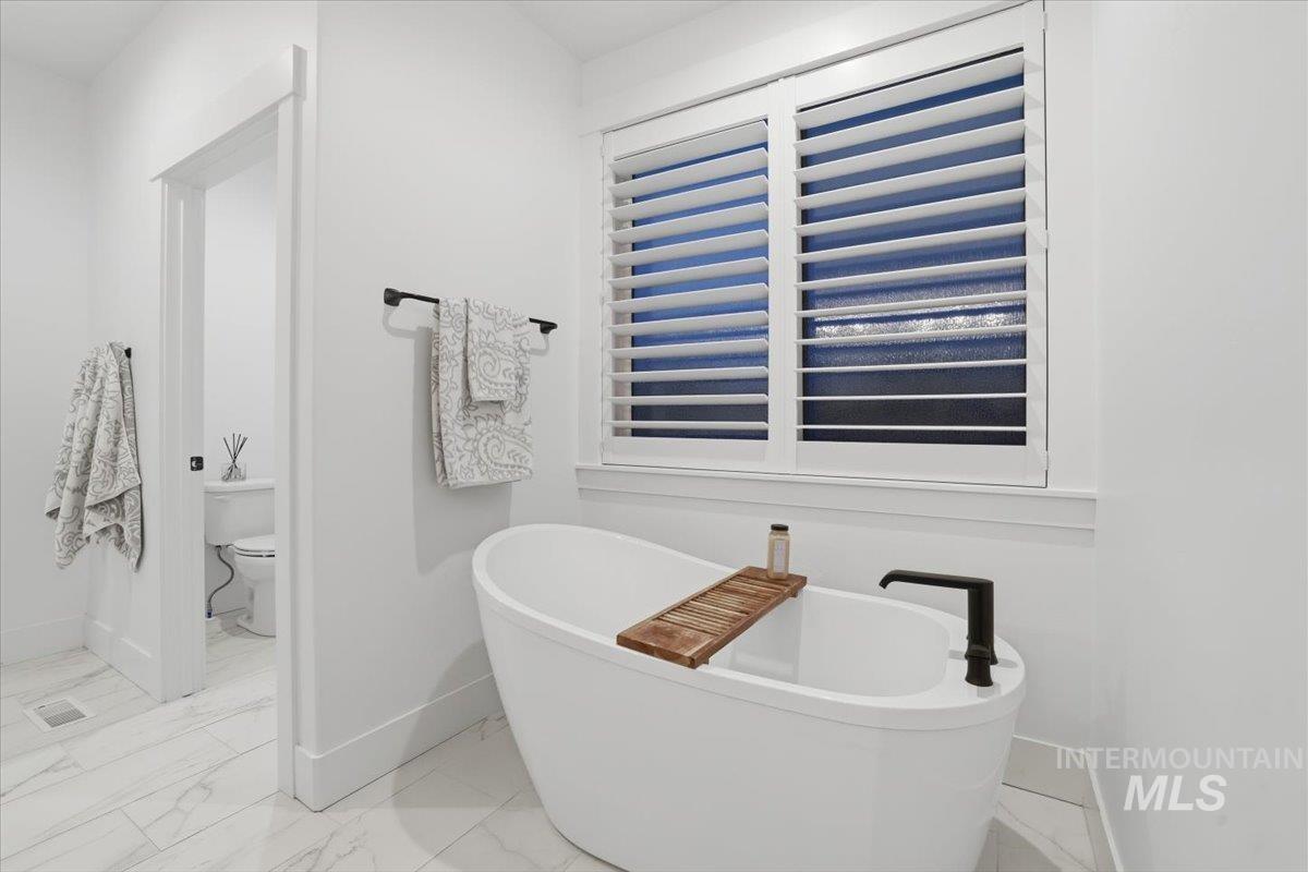 Full bath featuring a freestanding tub and light marble finish floors