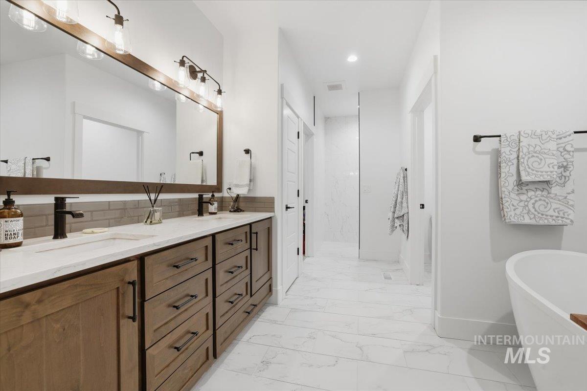 Bathroom featuring double vanity, a freestanding bath, light marble finish flooring, backsplash, and recessed lighting