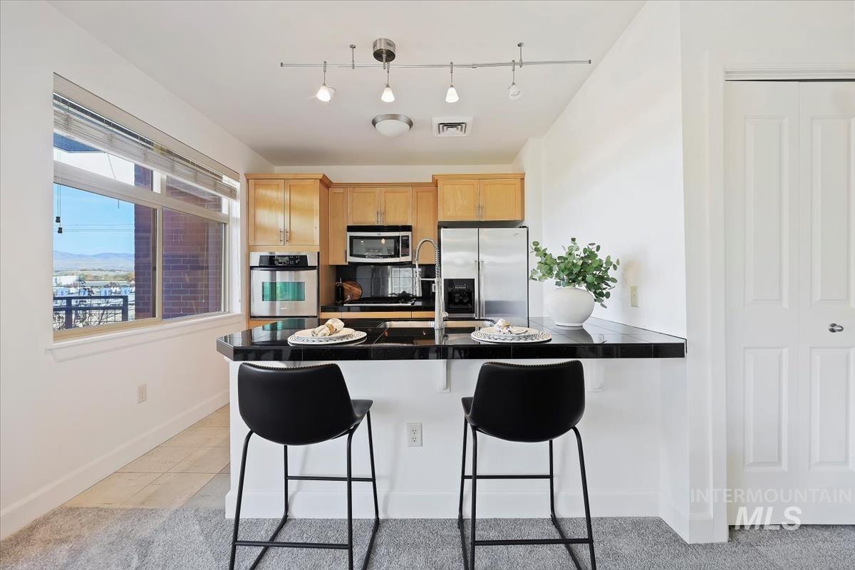 Kitchen with dark countertops, light tile patterned floors, a breakfast bar area, a peninsula, and stainless steel appliances