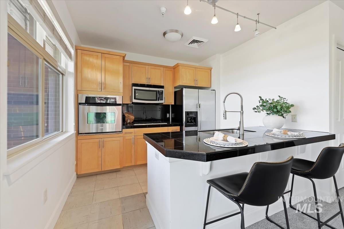 Kitchen with tile counters, a breakfast bar area, appliances with stainless steel finishes, backsplash, and light tile patterned floors