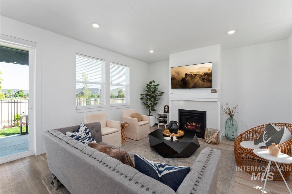 Spacious living area featuring light wood-finish flooring, a contemporary fireplace with a white mantel, and recessed lighting