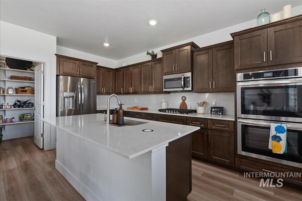Gourmet kitchen featuring a substantial island with countertop seating, stainless steel appliances, extensive dark wood cabinetry, a built-in double oven, and wood-finish flooring