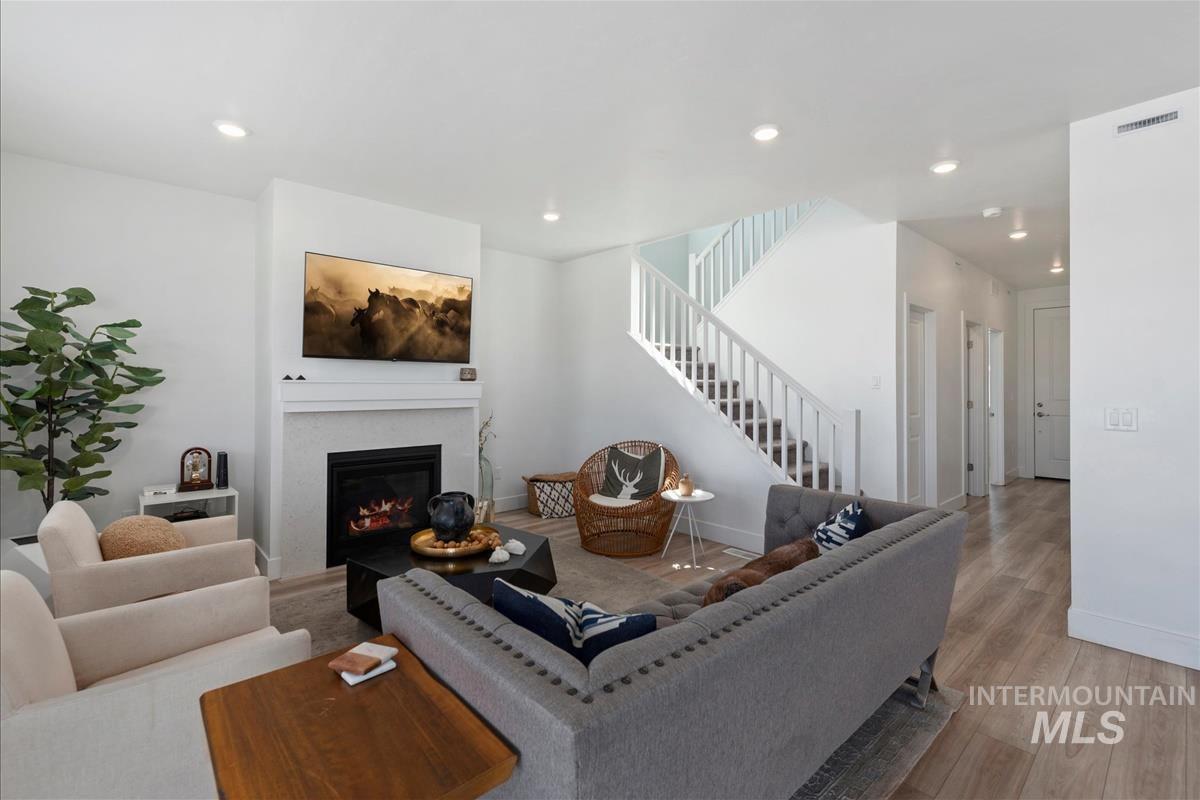 Living area featuring a fireplace with a textured surround, recessed lighting, wood-finish flooring, a white staircase with balusters, and a neutral color palette