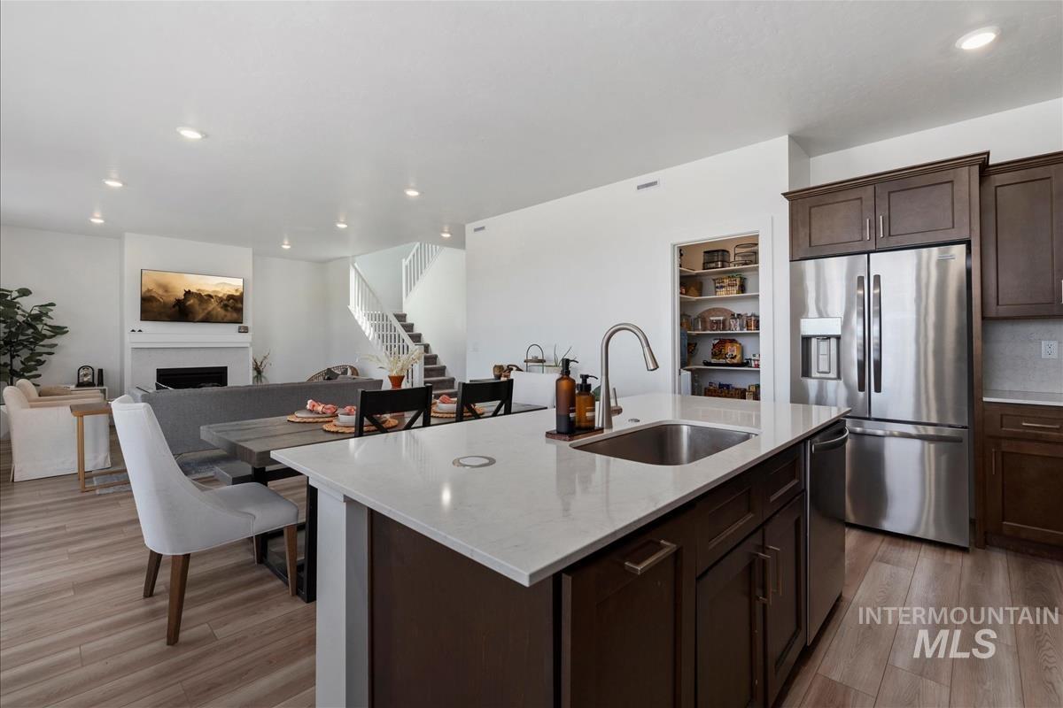 Open-concept kitchen featuring an island with a stainless steel sink and gooseneck faucet, light-toned countertops, and dark wood-finish cabinetry