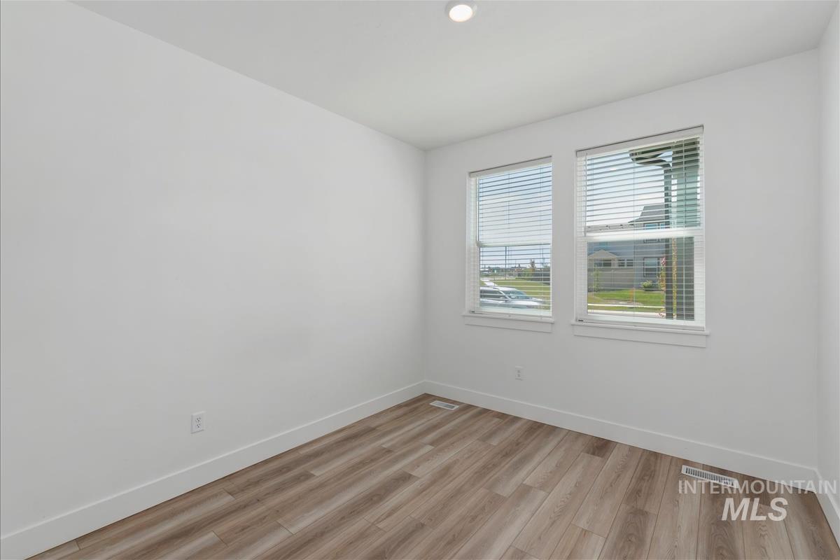 Bright room featuring two windows with blinds, wood-finish flooring, white walls, and recessed lighting
