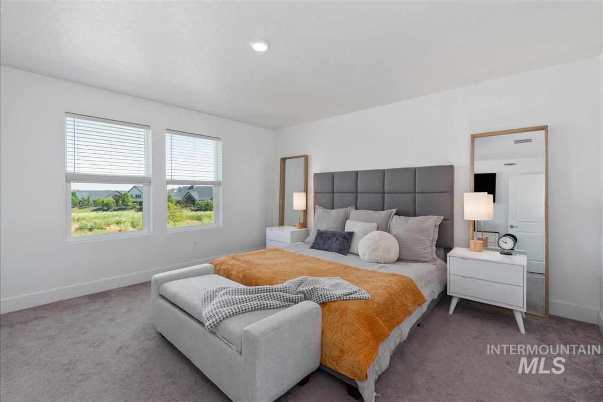 Recessed lighting illuminates a carpeted bedroom featuring two large windows with blinds and white trim, a paneled headboard, and white baseboards