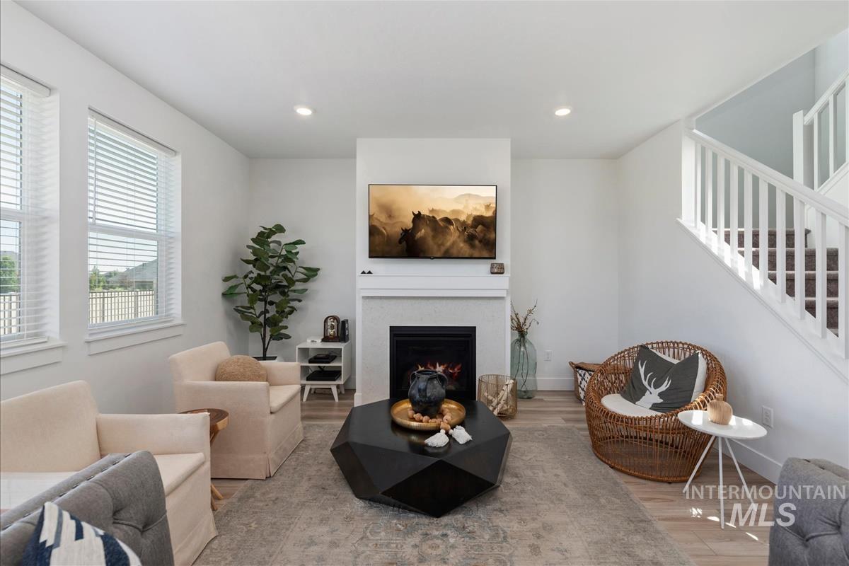 Spacious living area featuring light wood-finish flooring, a white mantel fireplace, and a staircase with white railings