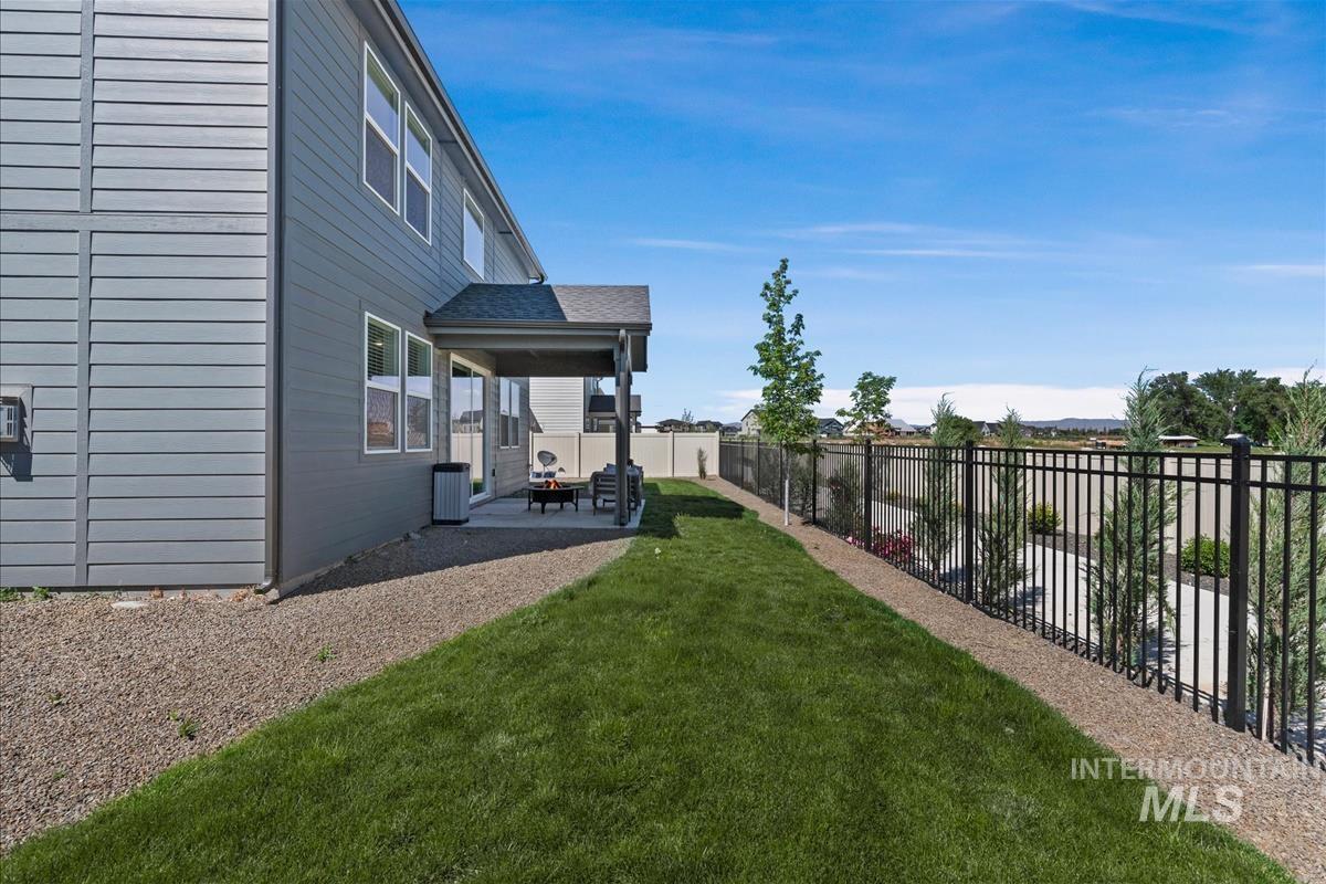 Expansive backyard featuring a covered patio, manicured lawn, gravel perimeter, and black metal fencing