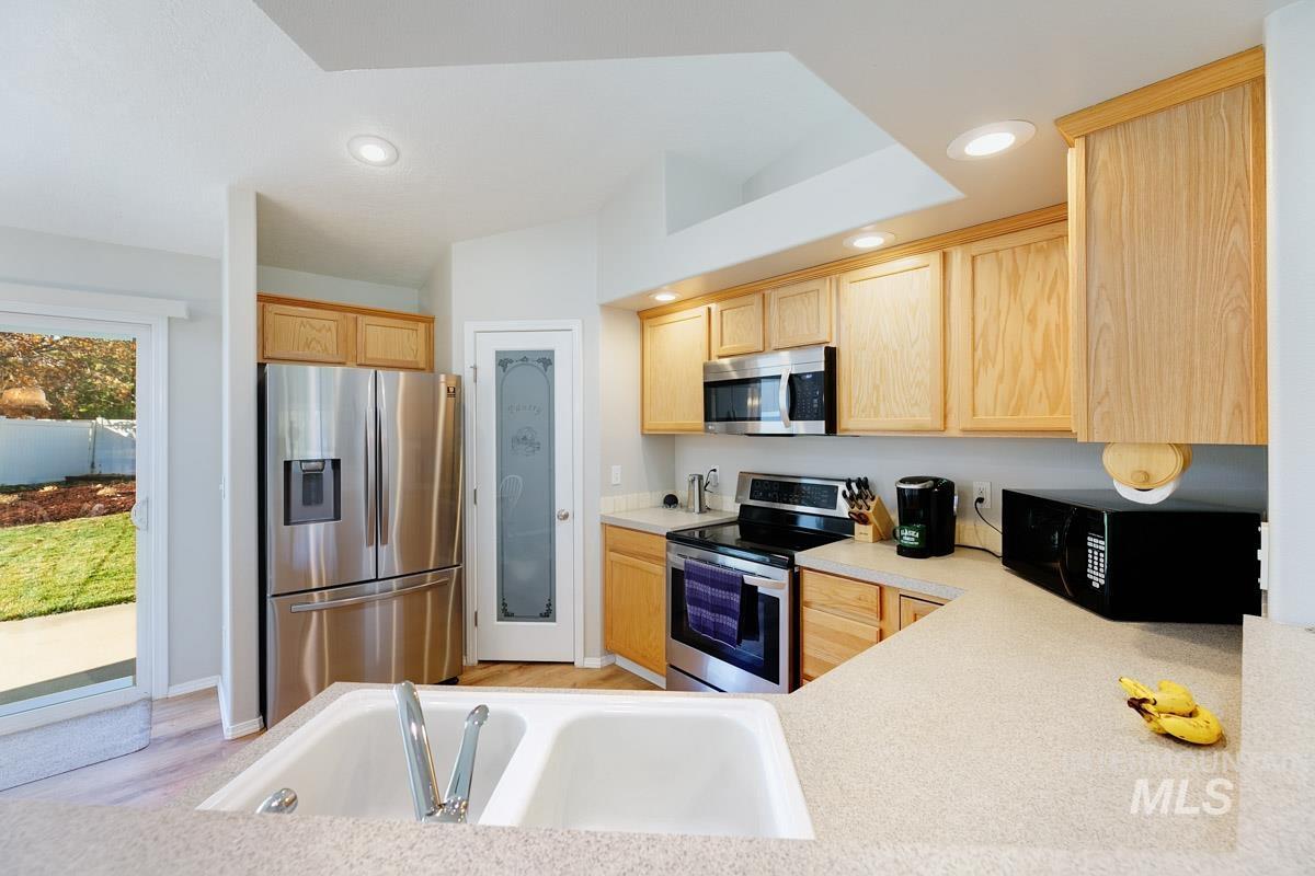Kitchen with light brown cabinetry, stainless steel appliances, light countertops, recessed lighting, and light wood finished floors