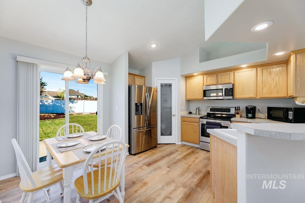 Kitchen with light countertops, appliances with stainless steel finishes, light wood finished floors, a chandelier, and hanging light fixtures
