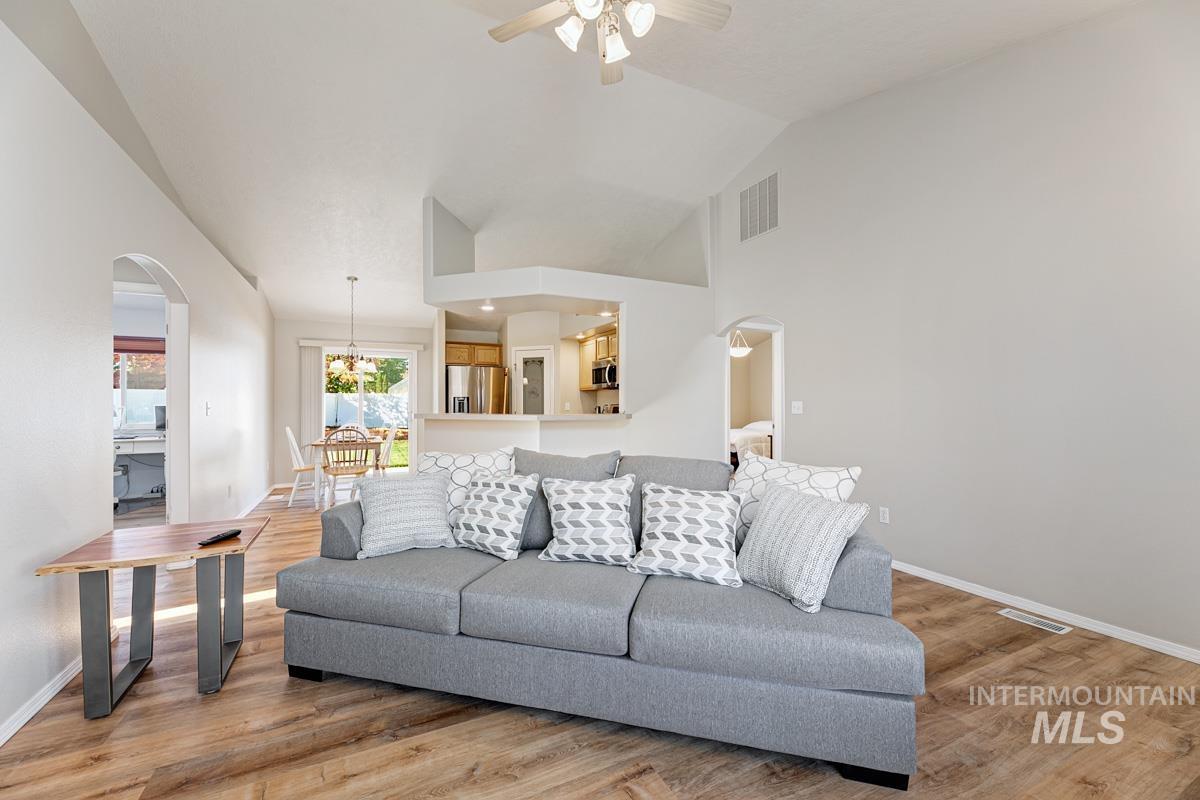 Living area with arched walkways, light wood-style floors, vaulted ceiling, a ceiling fan, and a chandelier