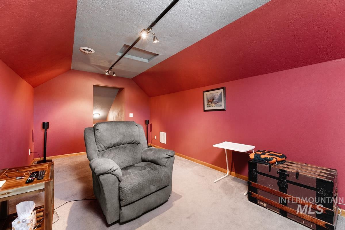 Sitting room with vaulted ceiling, track lighting, carpet floors, and a textured ceiling