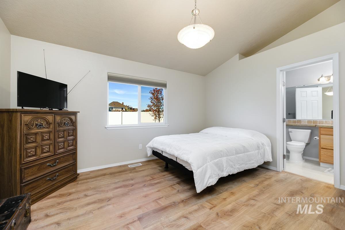 Bedroom featuring light wood finished floors, vaulted ceiling, and ensuite bath