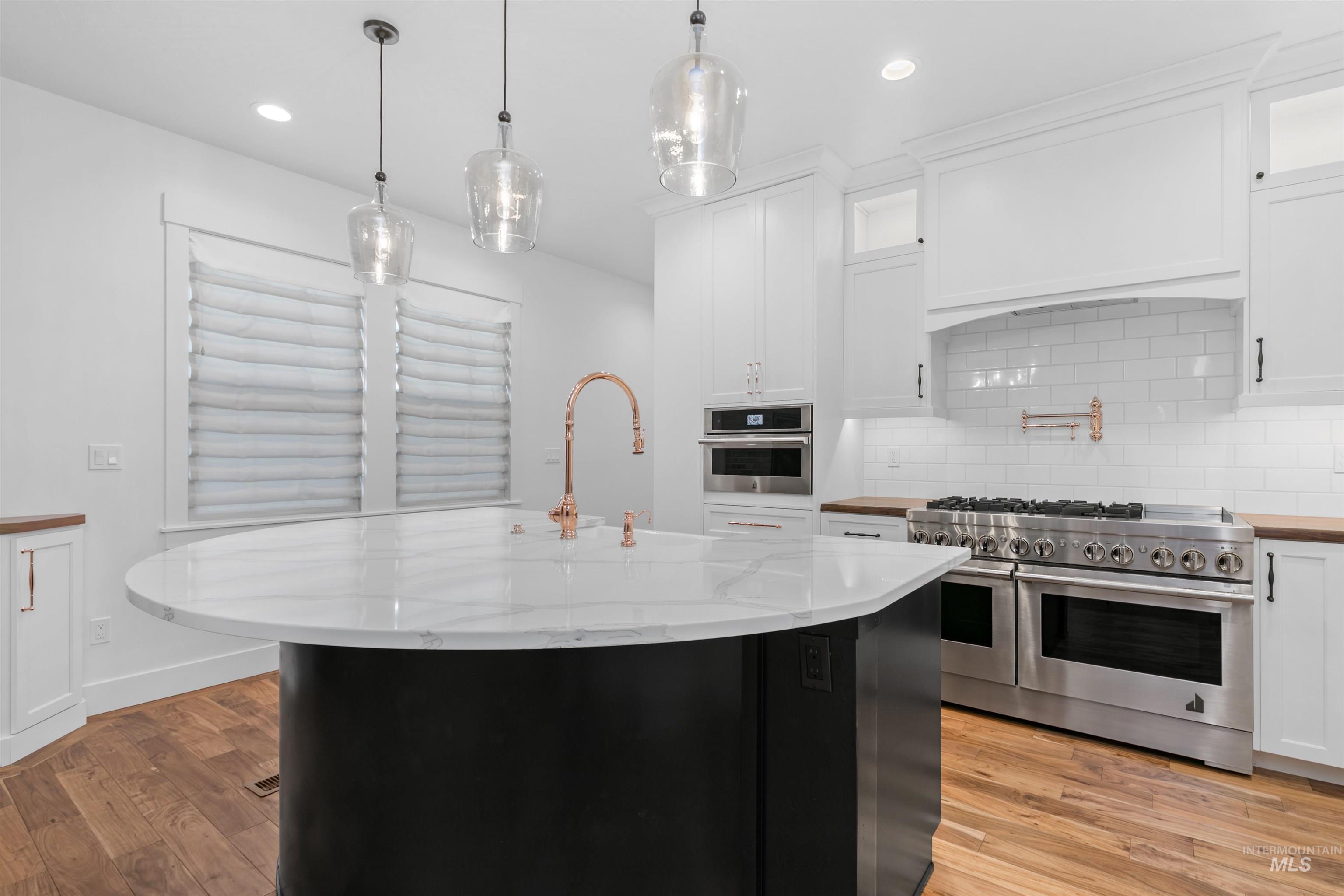 Kitchen with dark cabinetry, tasteful backsplash, a kitchen island with sink, stainless steel appliances, and pendant lighting