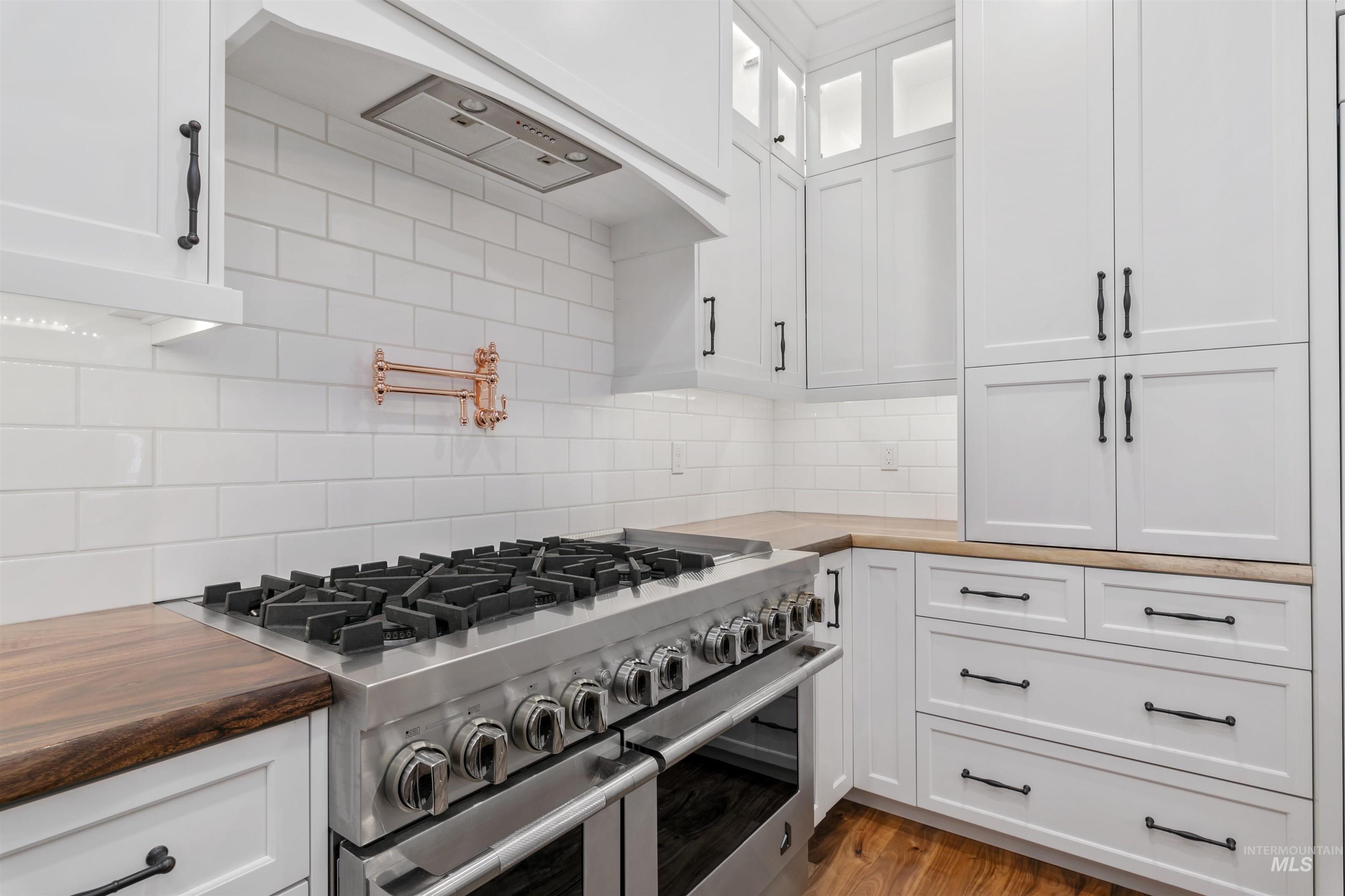 Kitchen featuring range with two ovens, tasteful backsplash, white cabinets, glass insert cabinets, and butcher block counters