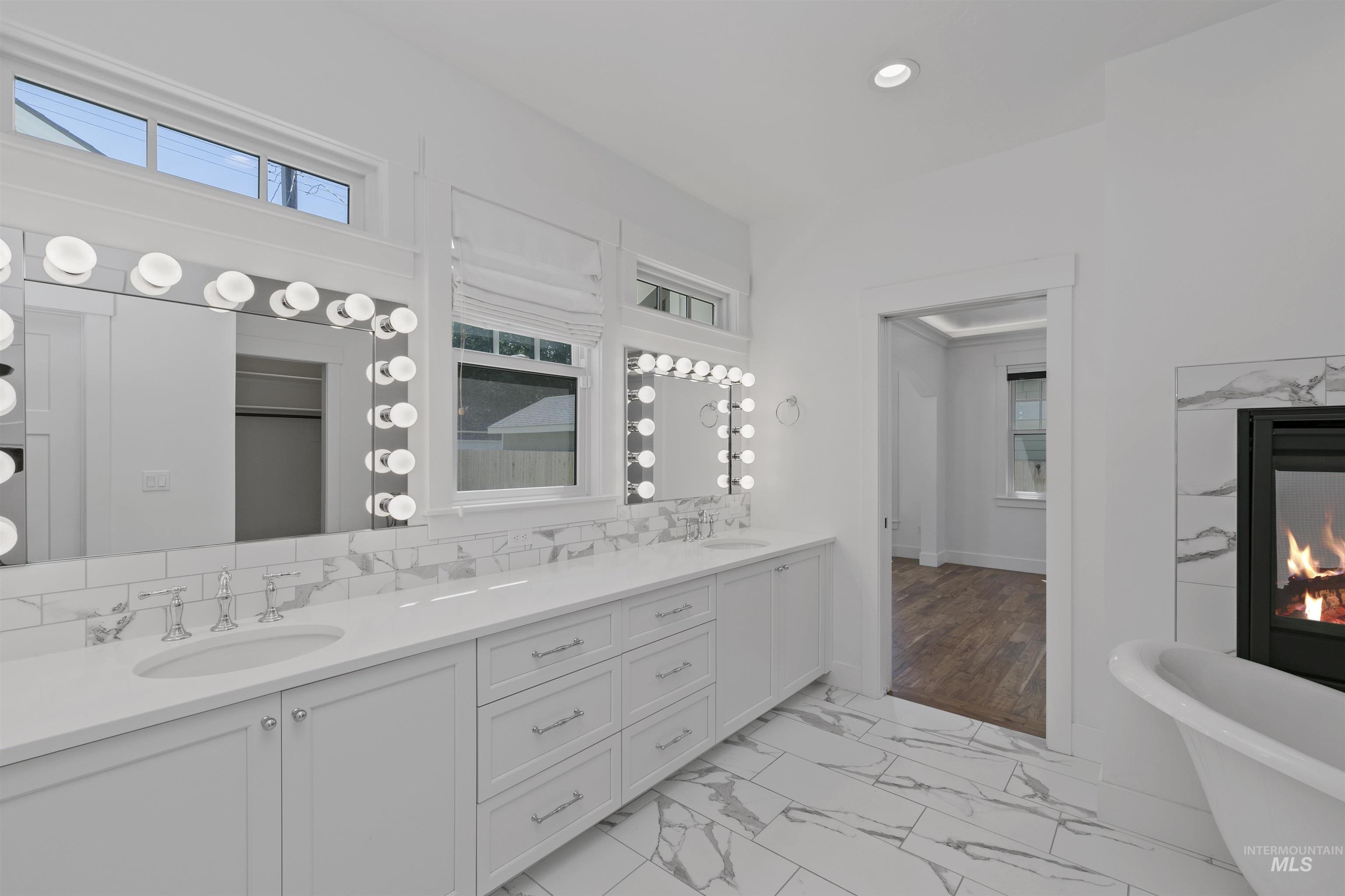 Bathroom with double vanity, a freestanding bath, recessed lighting, light marble finish flooring, and a fireplace