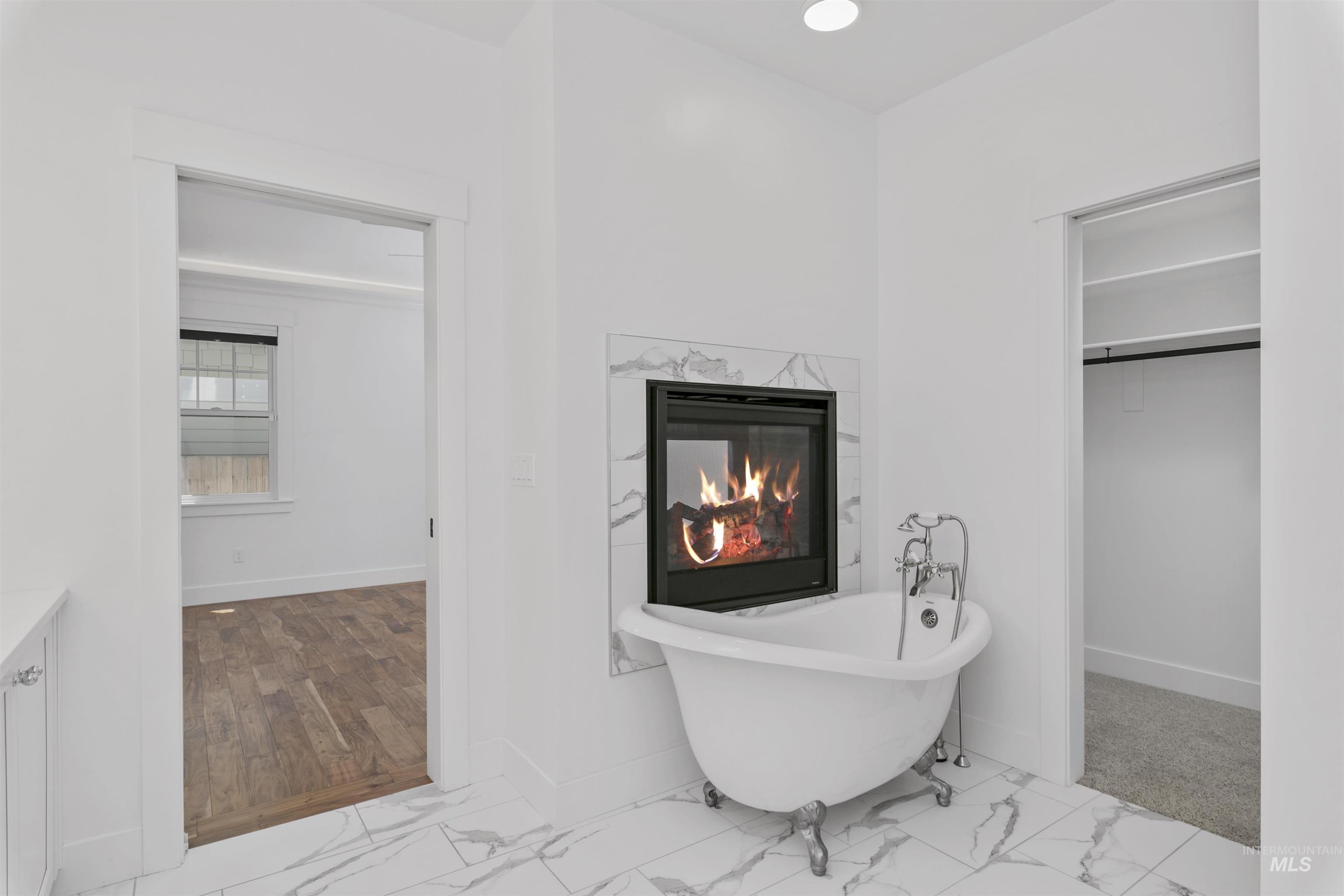 Full bath featuring a freestanding tub, light marble finish floors, a fireplace, vanity, and a walk in closet