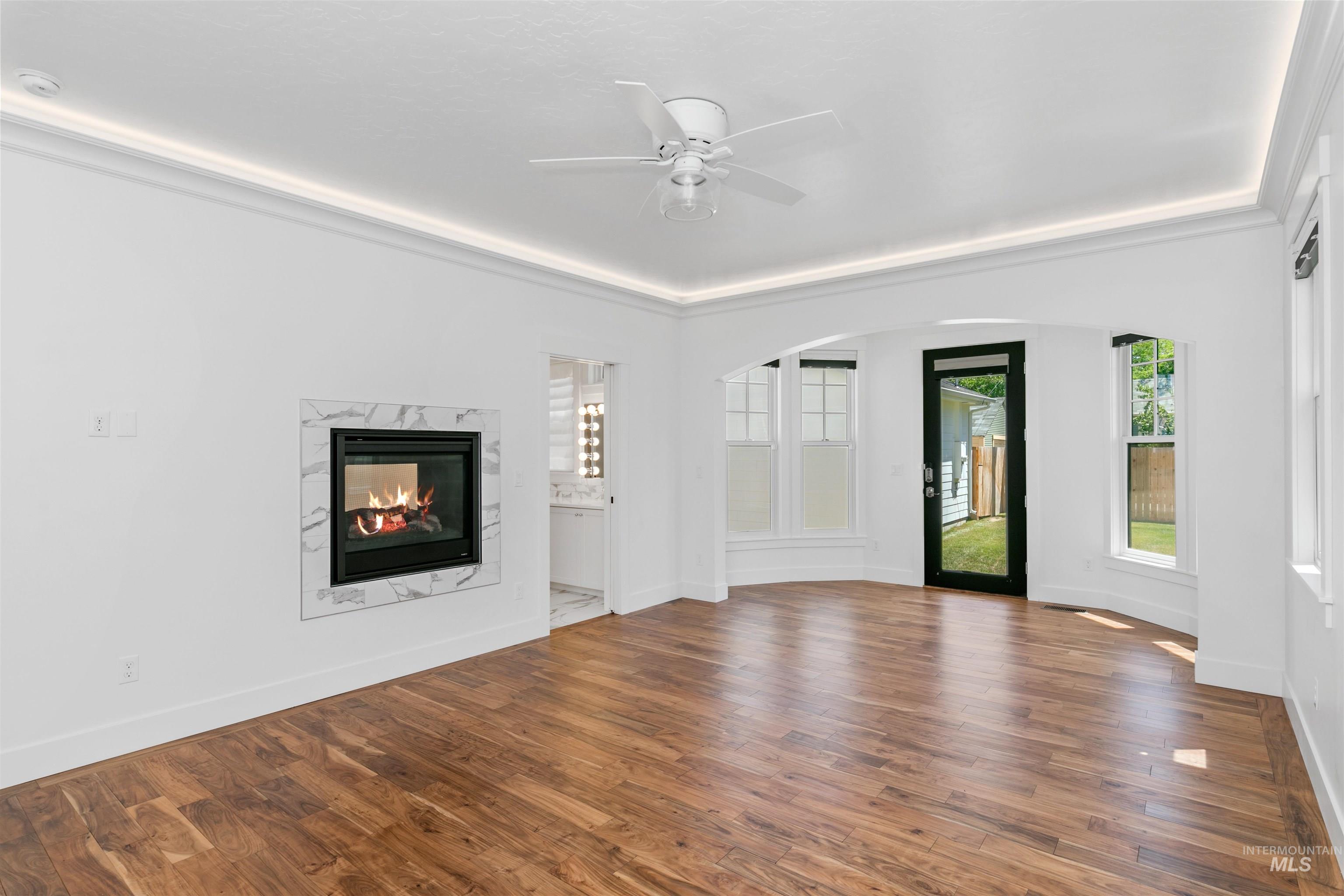 Unfurnished living room with wood finished floors, a fireplace, arched walkways, and ceiling fan