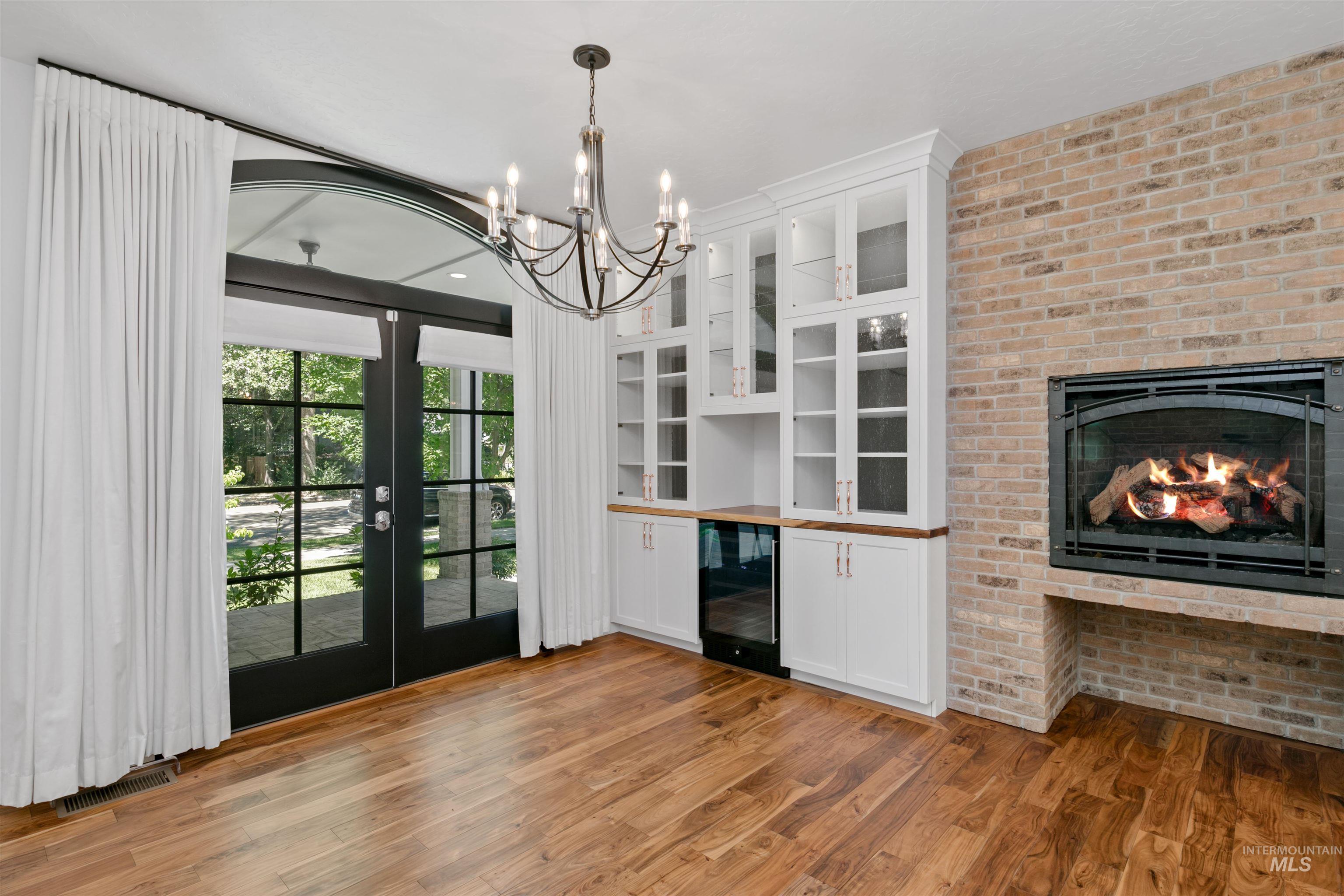 Unfurnished dining area featuring wine cooler, light wood finished floors, a fireplace, a chandelier, and brick wall