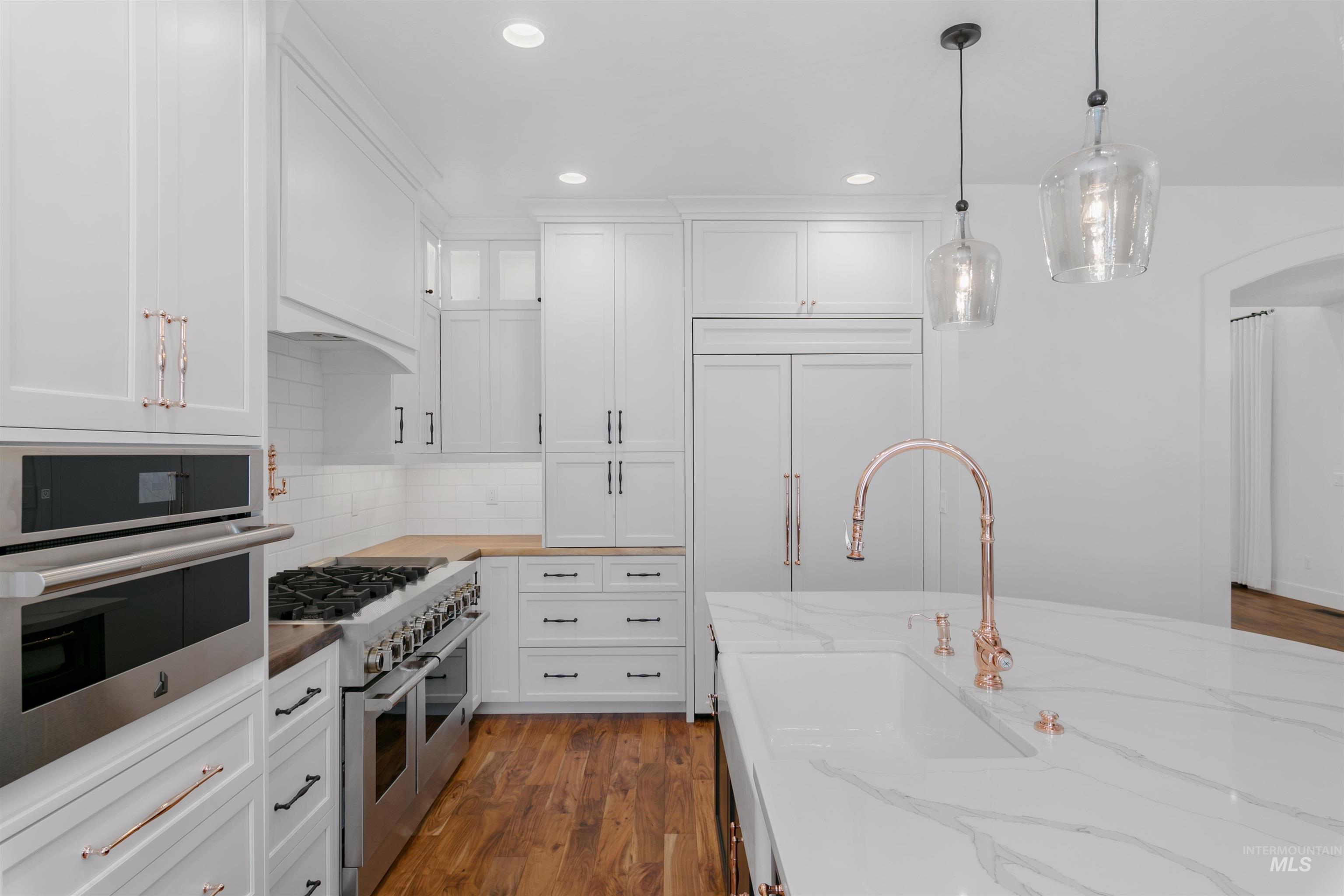 Kitchen featuring dark wood-type flooring, stainless steel appliances, white cabinetry, decorative light fixtures, and recessed lighting