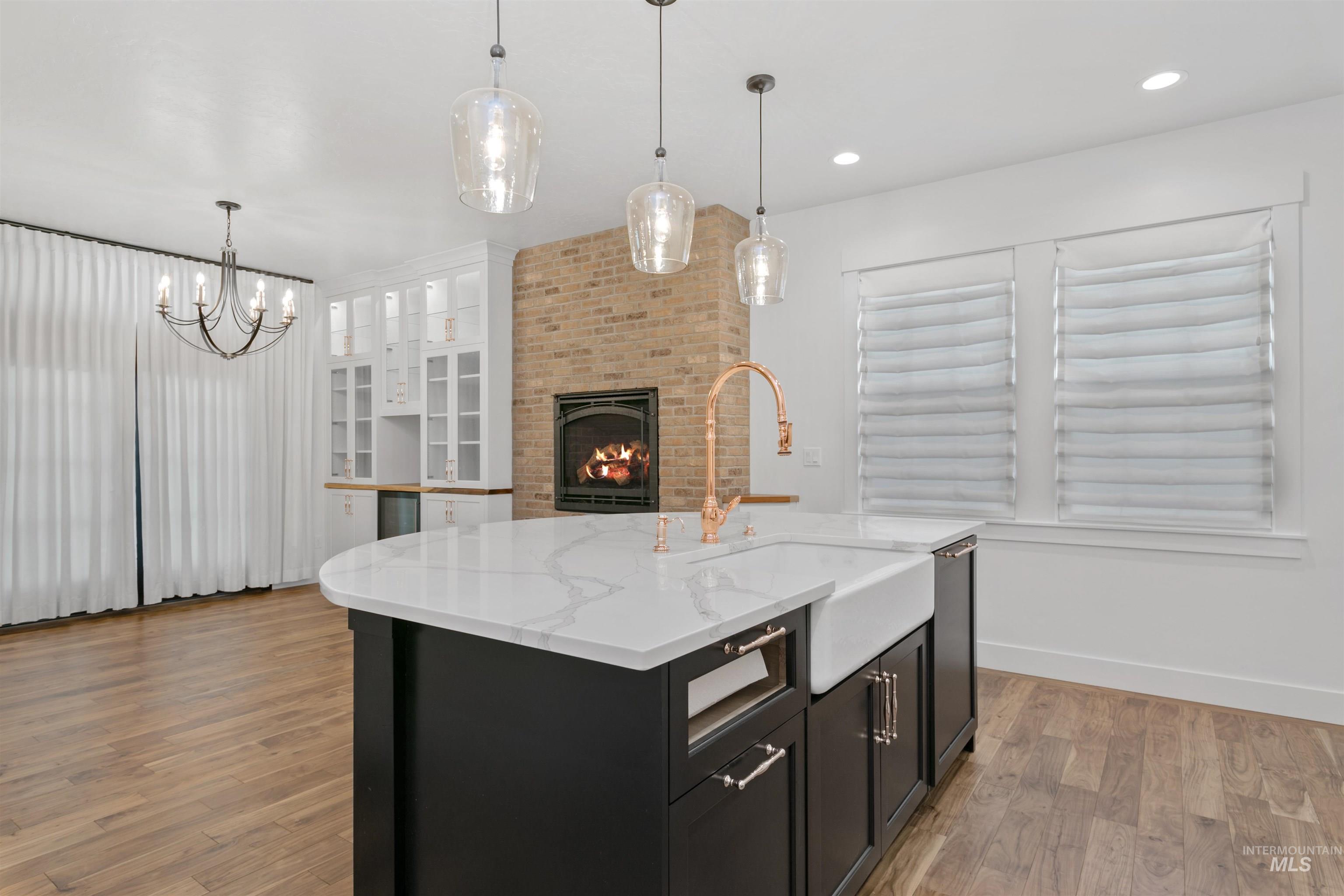 Kitchen with dark cabinetry, a fireplace, pendant lighting, glass insert cabinets, and an island with sink