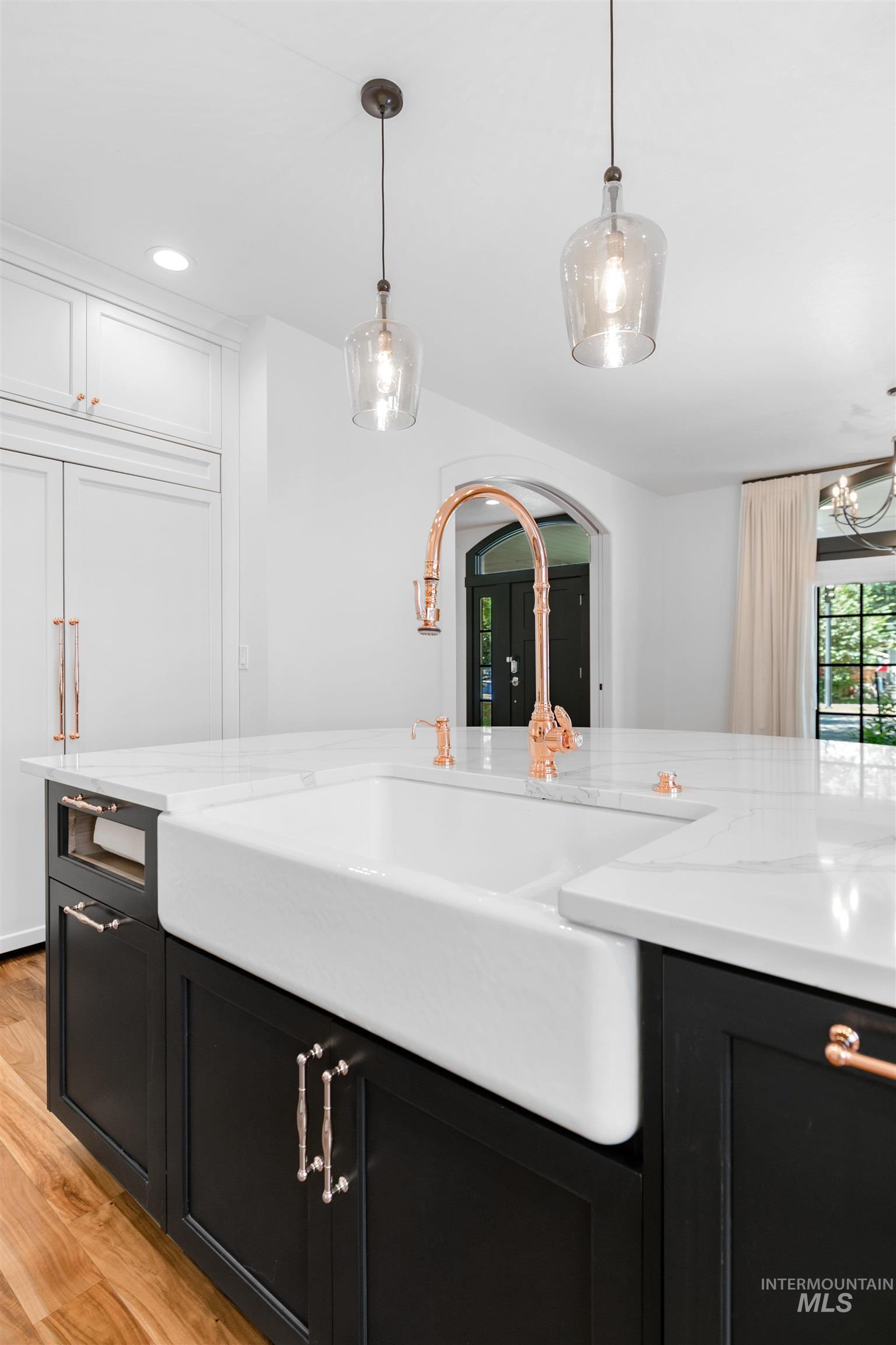 Kitchen with dark cabinetry, decorative light fixtures, light stone counters, light wood-style floors, and recessed lighting