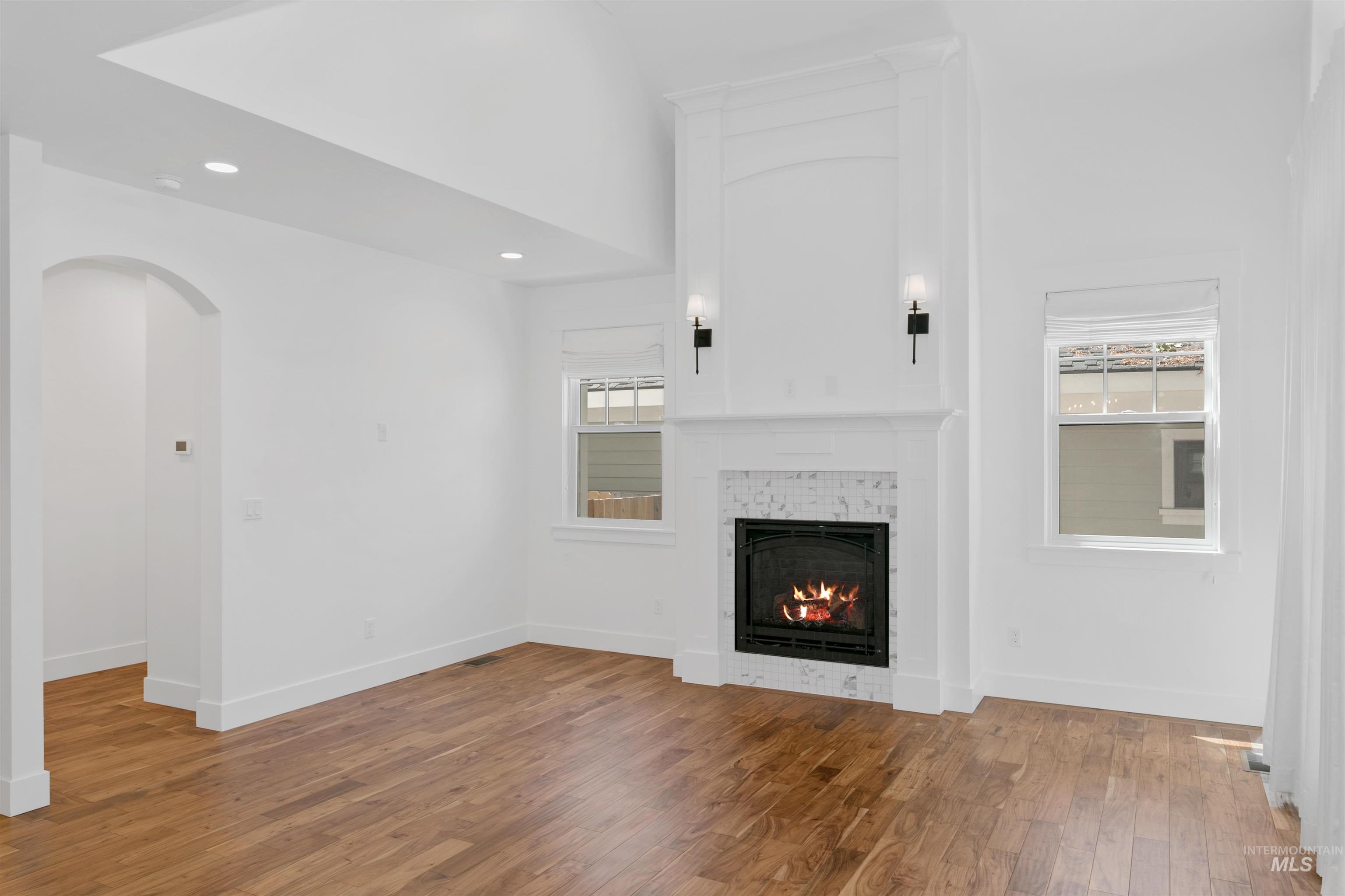 Unfurnished living room featuring healthy amount of natural light, light wood finished floors, a tile fireplace, recessed lighting, and a towering ceiling