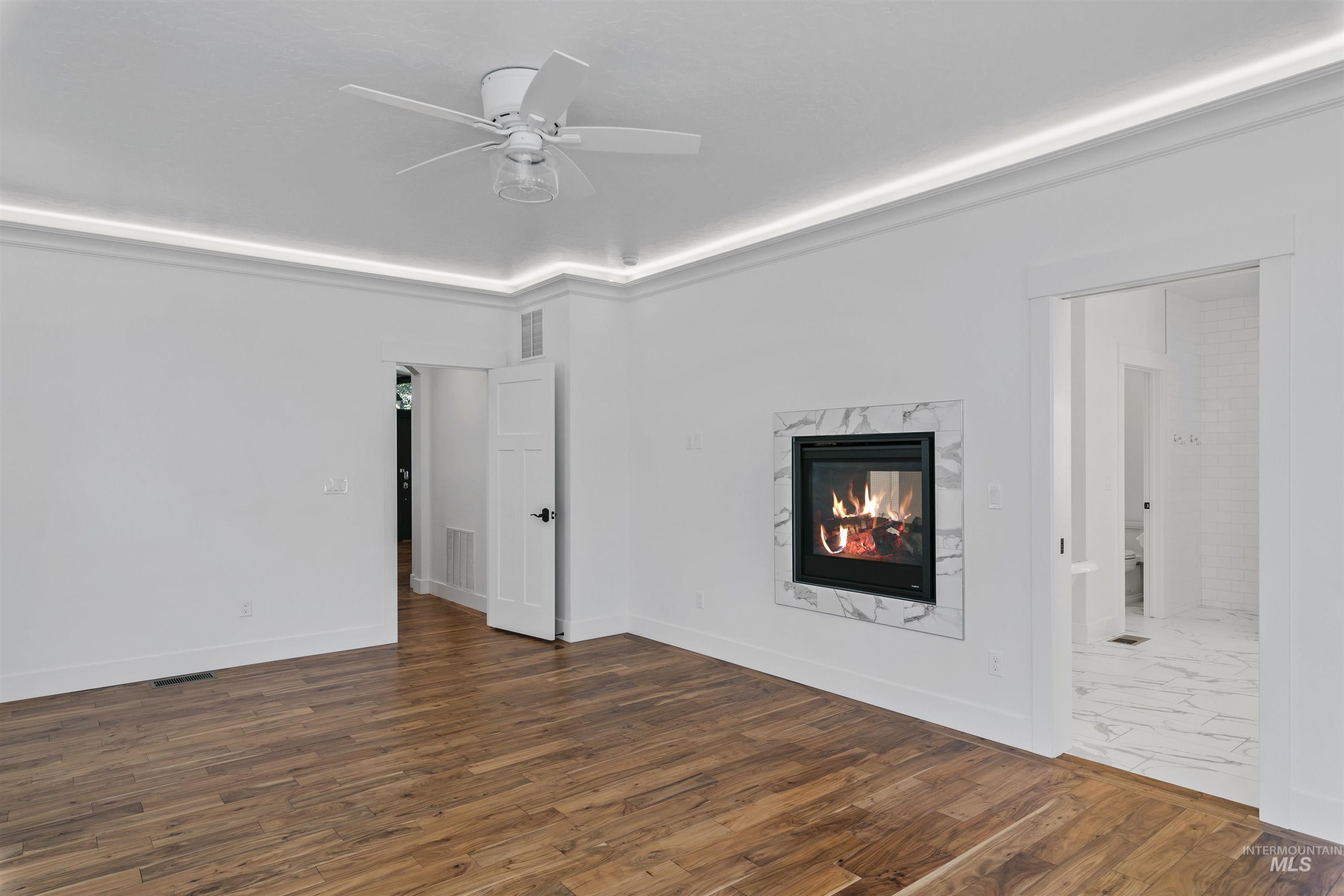 Unfurnished living room featuring dark wood-type flooring, a premium fireplace, and a ceiling fan