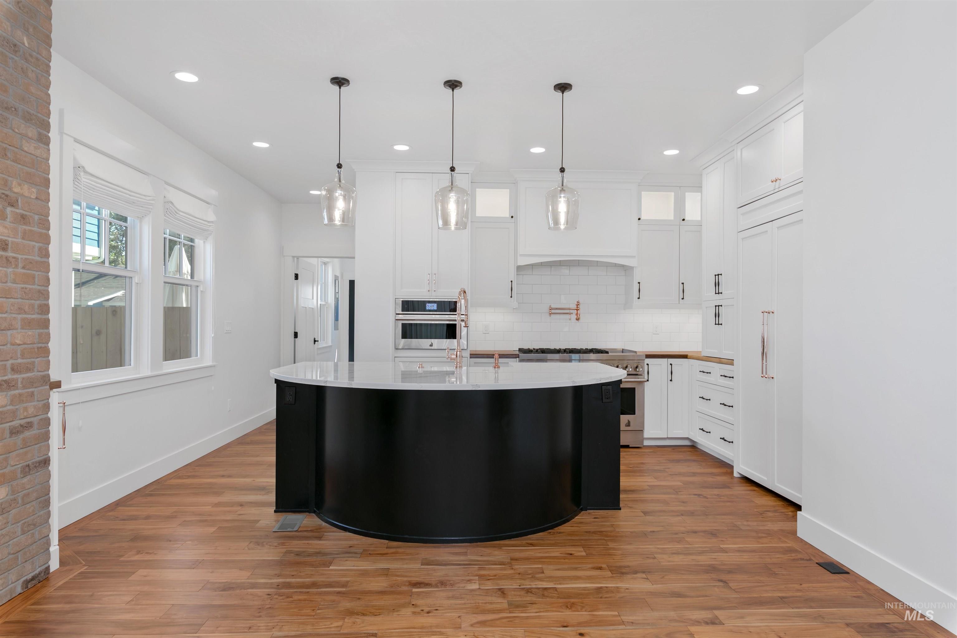 Kitchen with glass insert cabinets, white cabinetry, an island with sink, backsplash, and recessed lighting