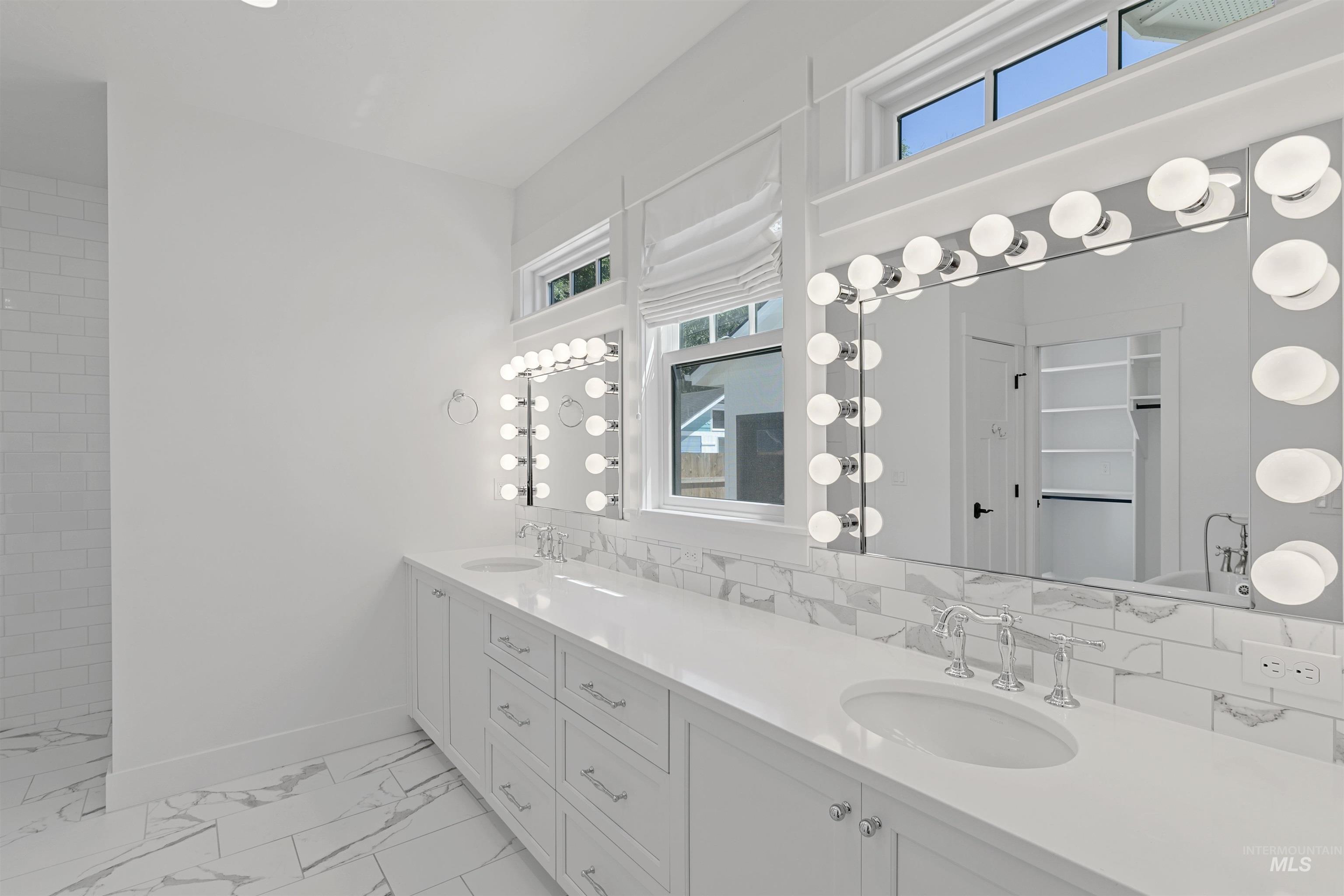 Full bath featuring double vanity, light marble finish flooring, backsplash, and a shower