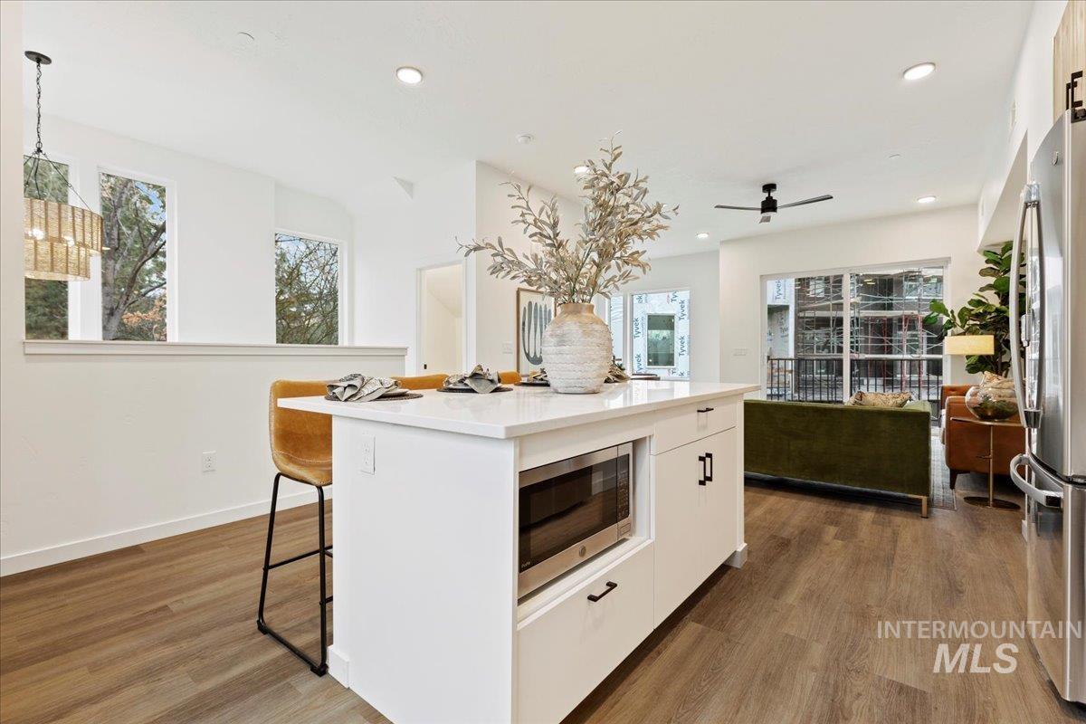 Kitchen with appliances with stainless steel finishes, white cabinetry, a kitchen island, dark wood-style floors, and light stone counters