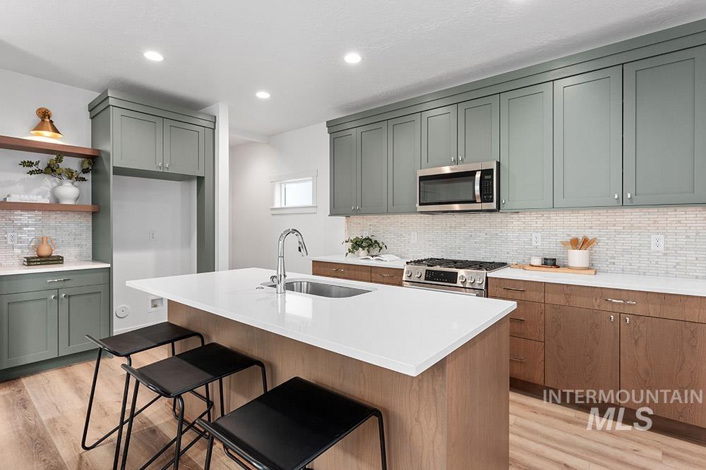 Kitchen with light wood finished floors, stainless steel appliances, decorative backsplash, light countertops, and recessed lighting