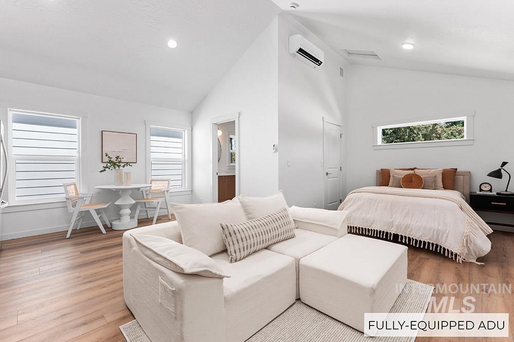 Bedroom with high vaulted ceiling, light wood-type flooring, recessed lighting, a wall unit AC, and ensuite bathroom