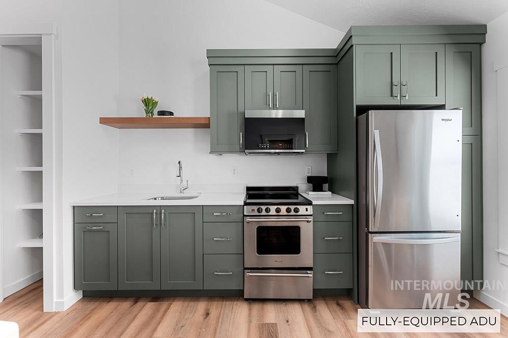 Kitchen with appliances with stainless steel finishes, light countertops, open shelves, light wood-style flooring, and green cabinets