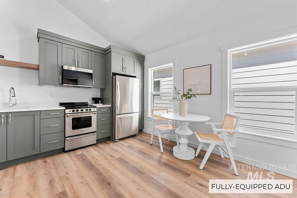 Kitchen featuring vaulted ceiling, stainless steel appliances, gray cabinets, light countertops, and light wood-style floors