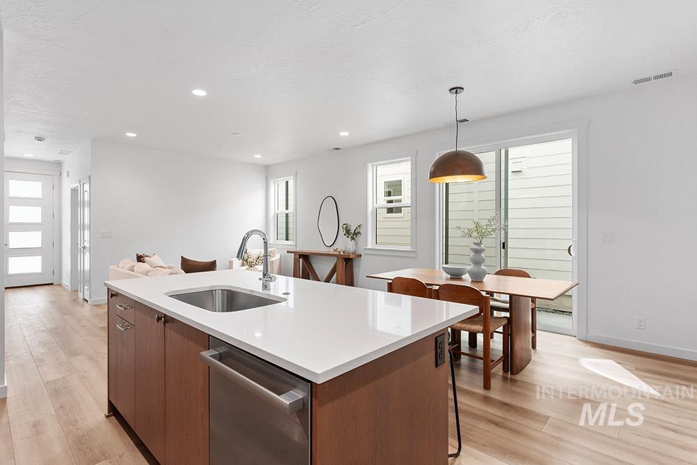 Kitchen featuring a kitchen island with sink, stainless steel dishwasher, light wood finished floors, light countertops, and recessed lighting