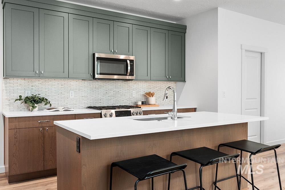 Kitchen featuring light wood finished floors, appliances with stainless steel finishes, backsplash, light countertops, and a textured ceiling