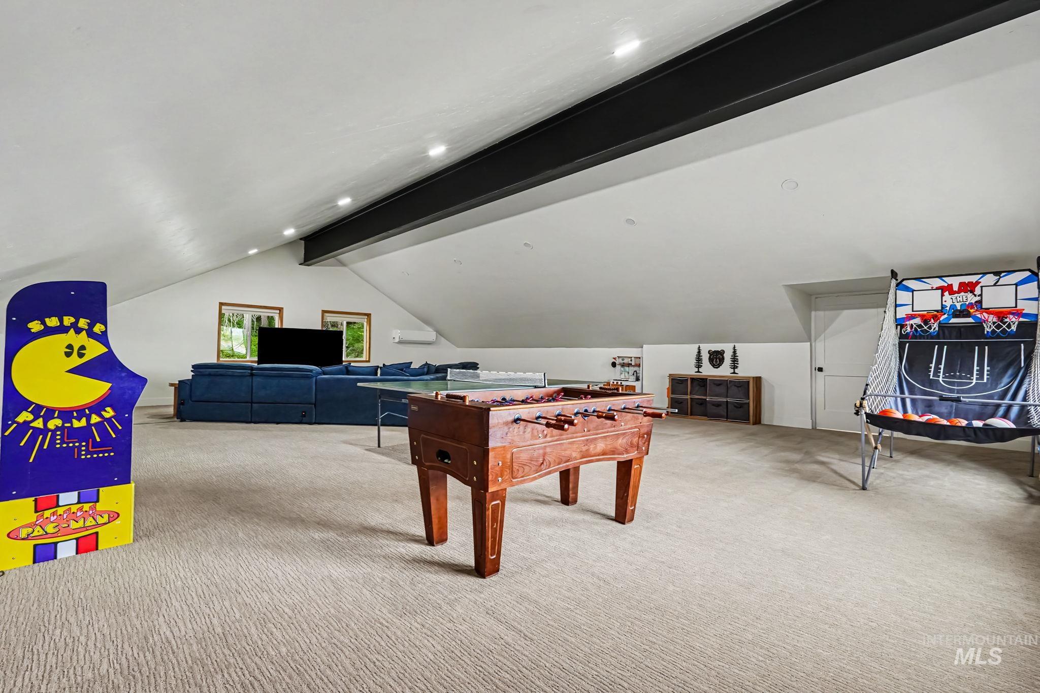 Spacious recreation room featuring sloped ceilings, recessed lighting, carpeted flooring, and exposed structural beam details