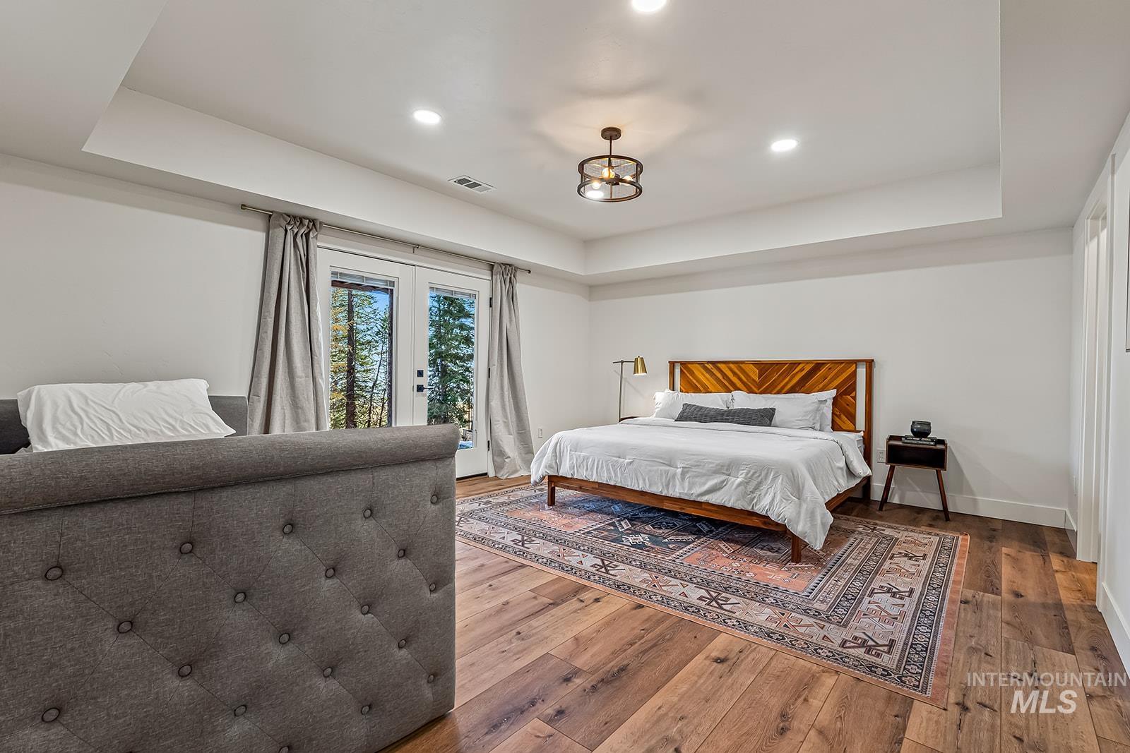Bedroom featuring light wood-type flooring, french doors, access to exterior, a raised ceiling, and recessed lighting