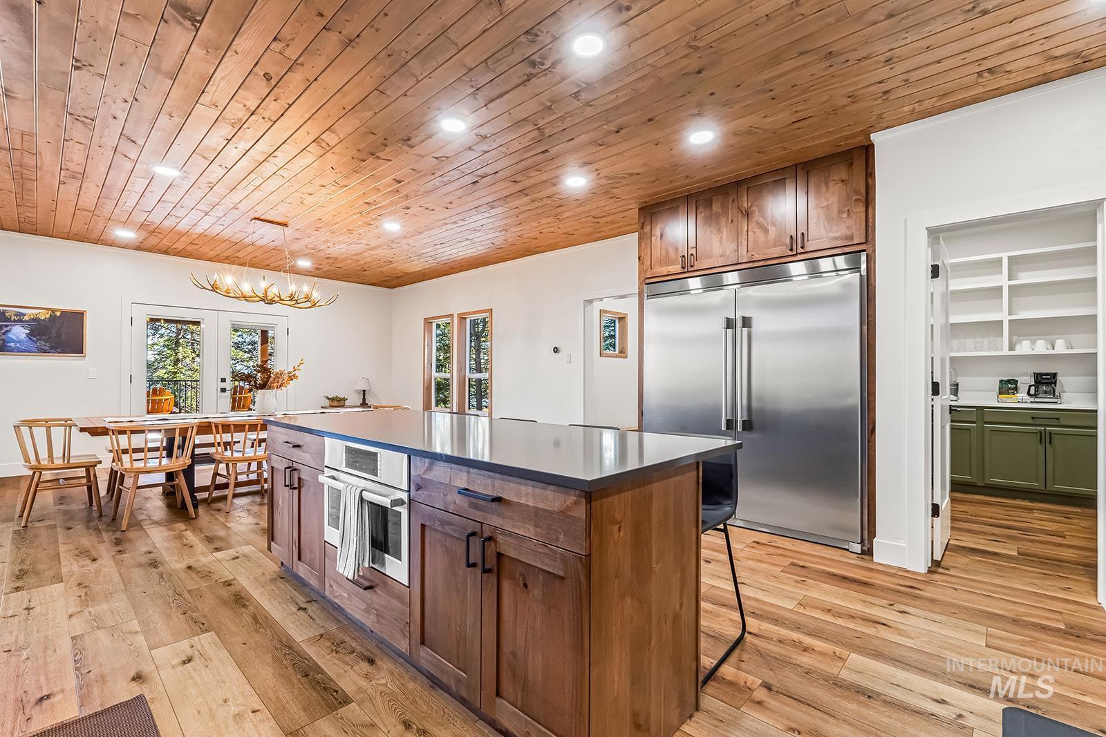 Kitchen with wood ceiling, stainless steel appliances, a kitchen island, dark countertops, and light wood-style flooring
