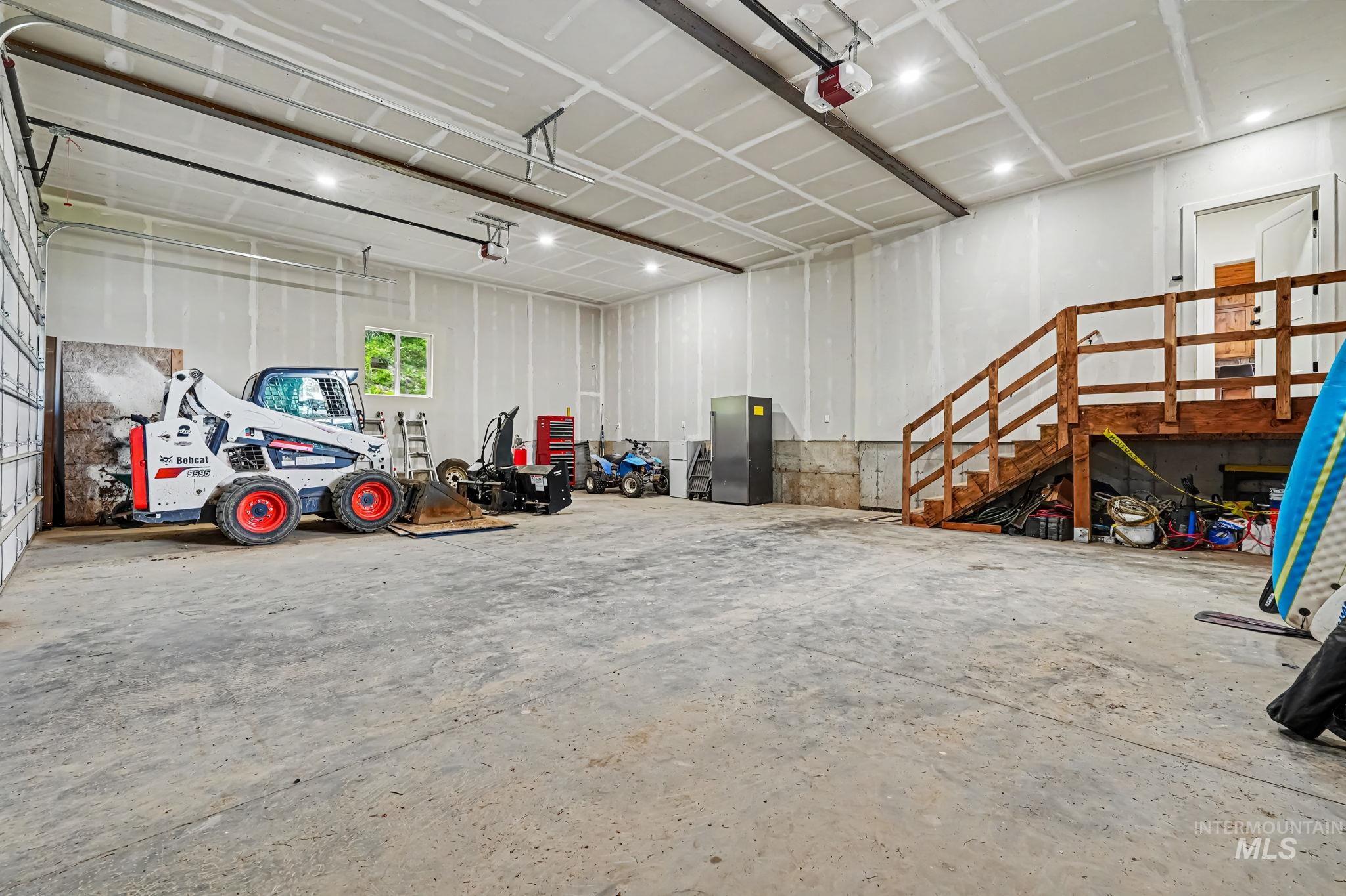 Spacious garage featuring a concrete floor, high ceilings with recessed lighting, two overhead garage doors, and an interior wood staircase with railing access to an upper level