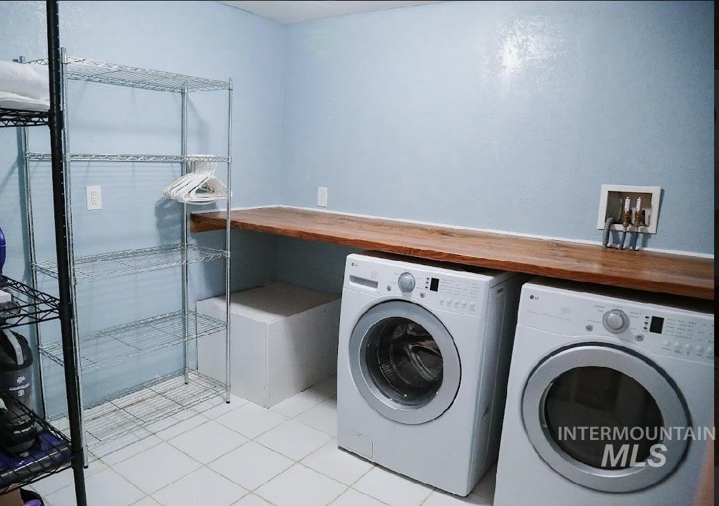 Washroom with washing machine and clothes dryer and light tile patterned flooring
