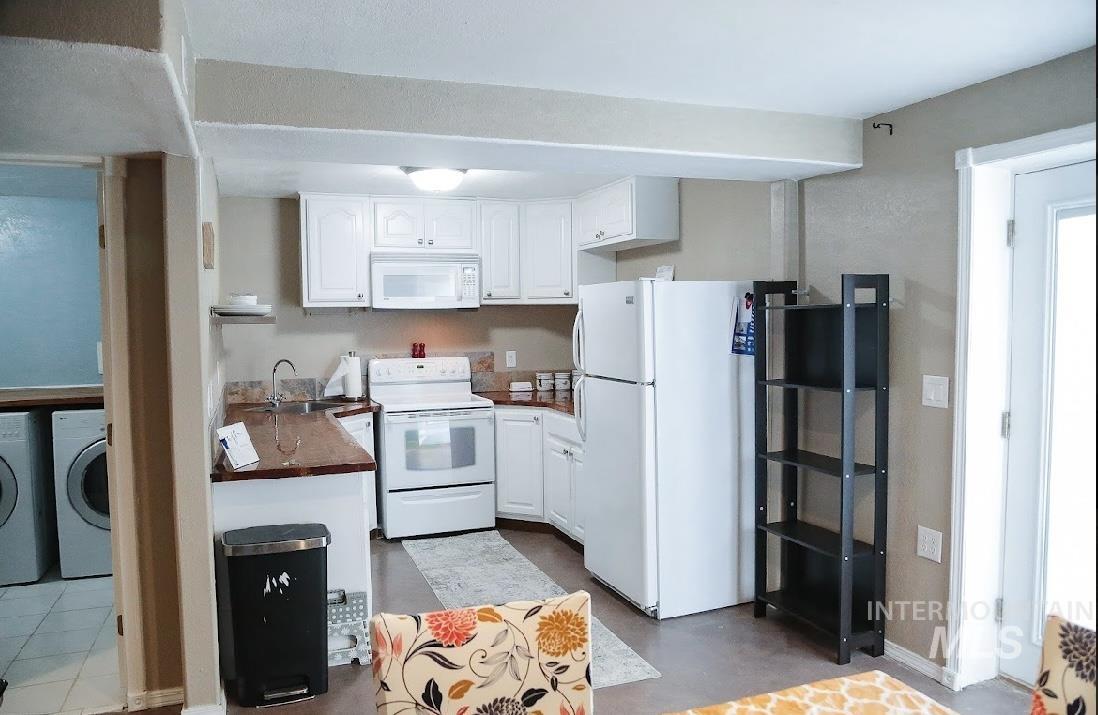 Kitchen with white appliances, white cabinetry, dark countertops, and washer and clothes dryer