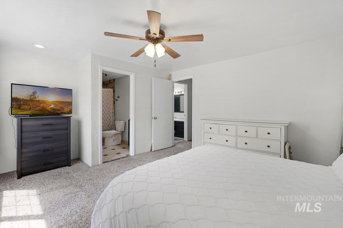 Carpeted bedroom featuring connected bathroom and a ceiling fan