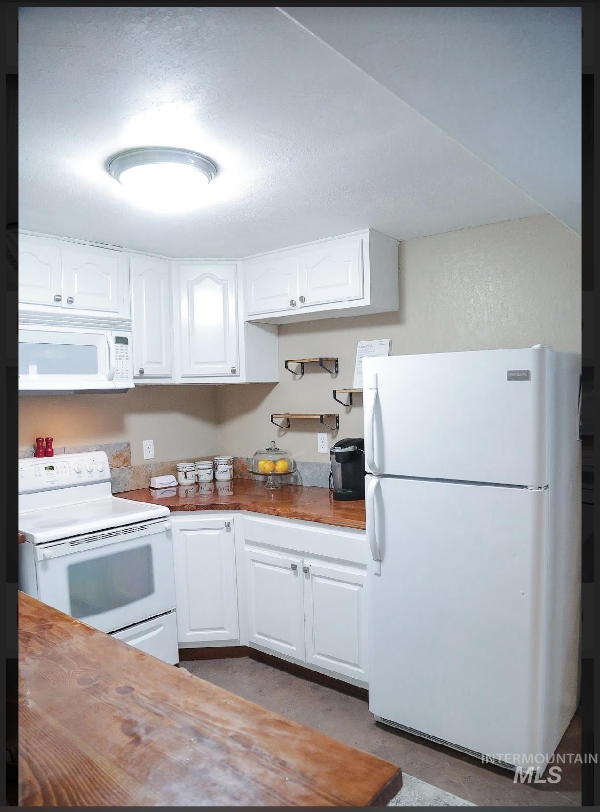Kitchen featuring white appliances, wood counters, and white cabinets