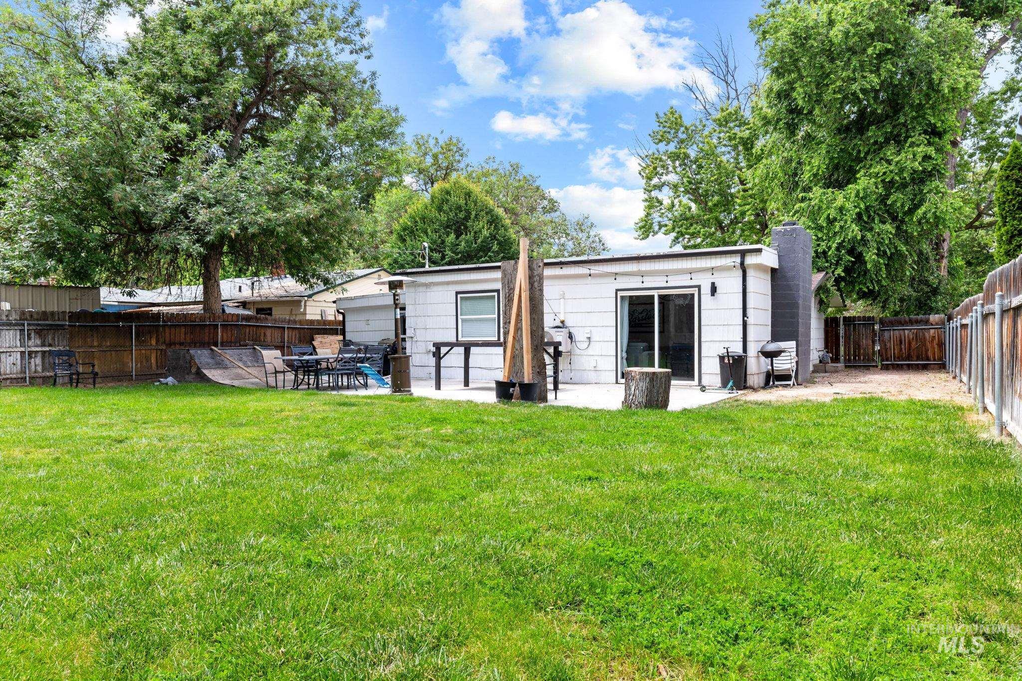 Expansive backyard featuring a lush lawn, concrete patio, sliding glass door access, exterior wall lighting, and a fenced perimeter