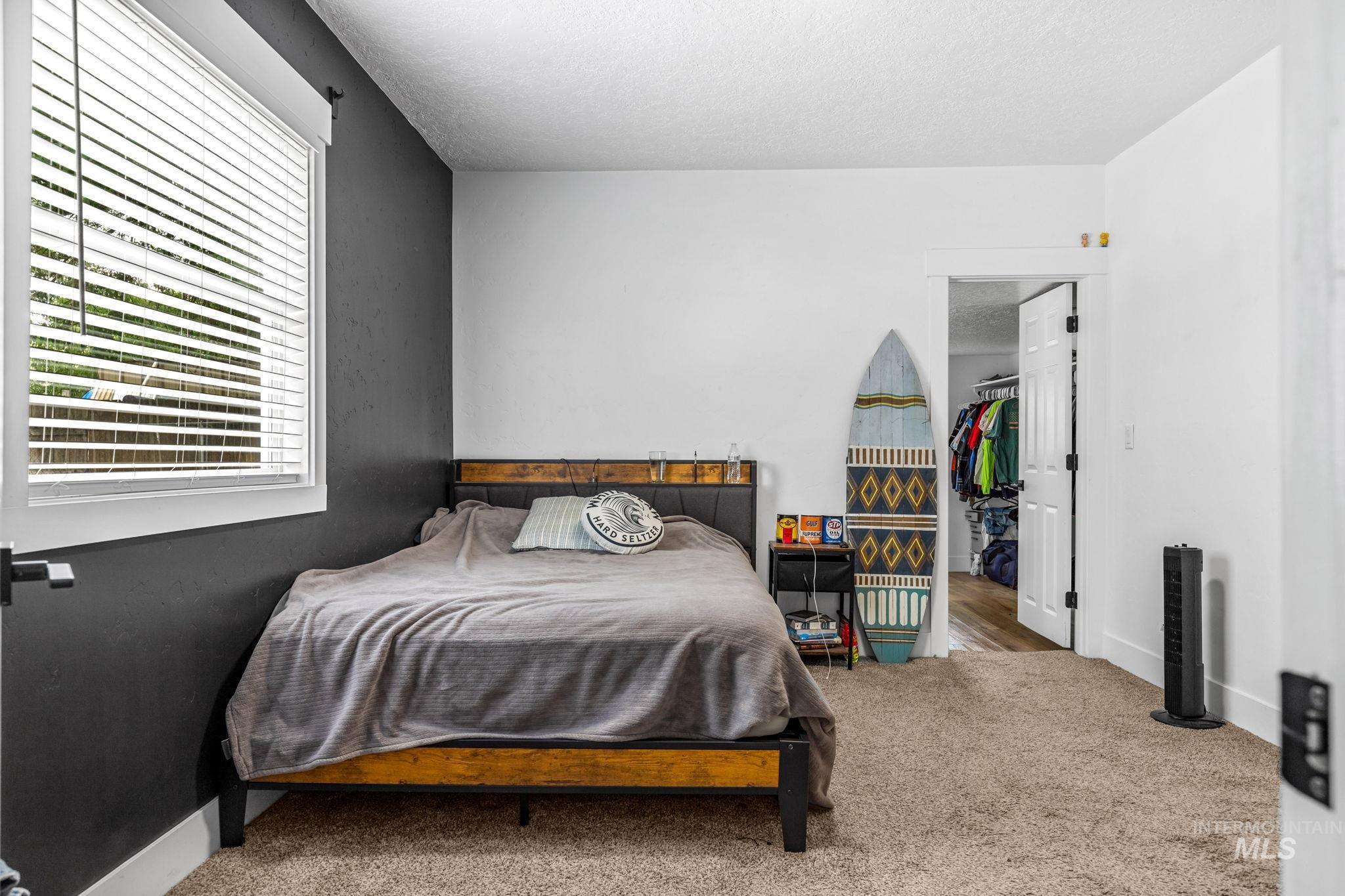 Carpeted bedroom featuring a window with white blinds, a two-tone wall design, and a doorway leading to a closet space