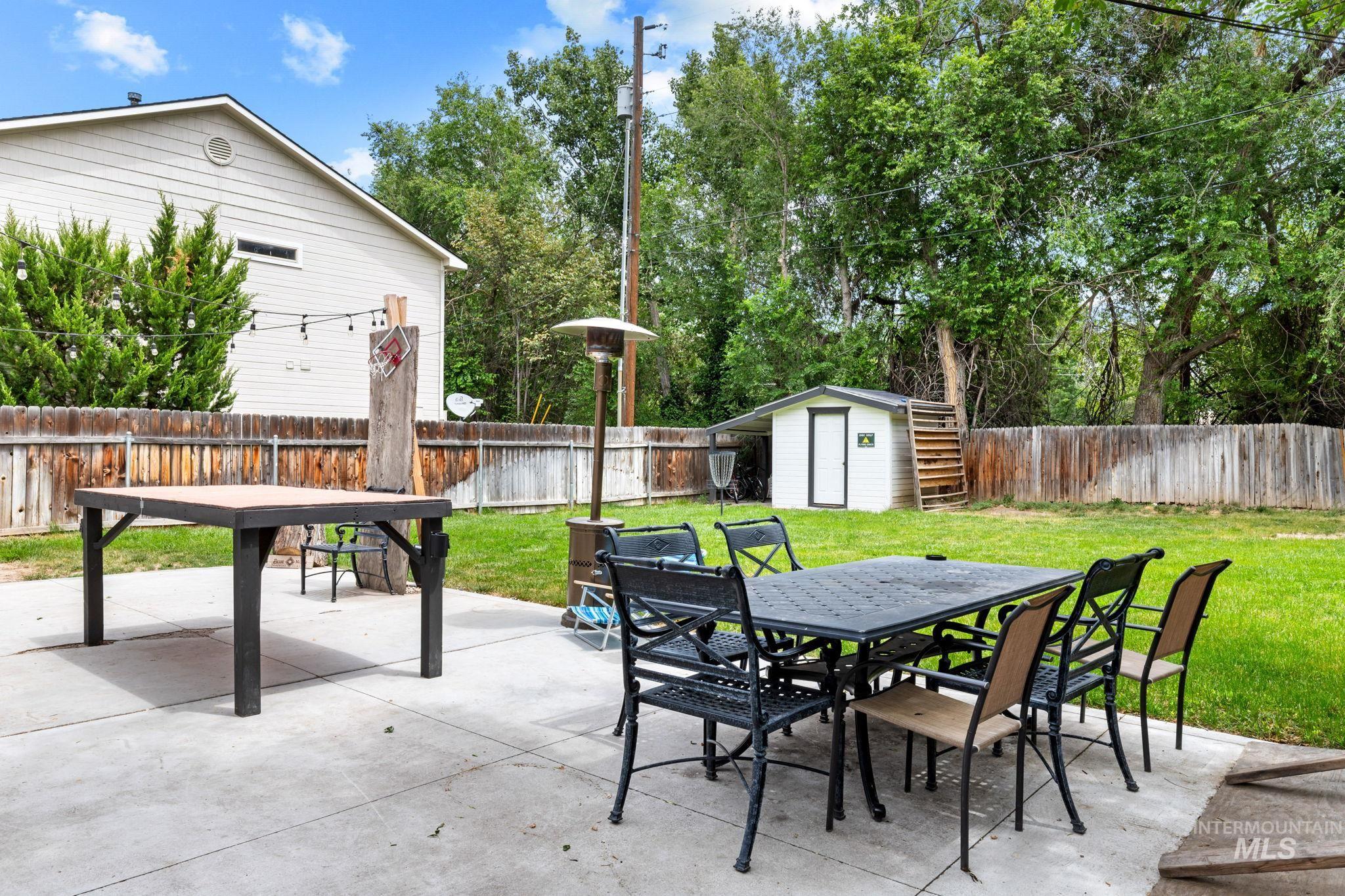 Expansive backyard featuring a large concrete patio, mature trees, a wood privacy fence, and a detached storage shed