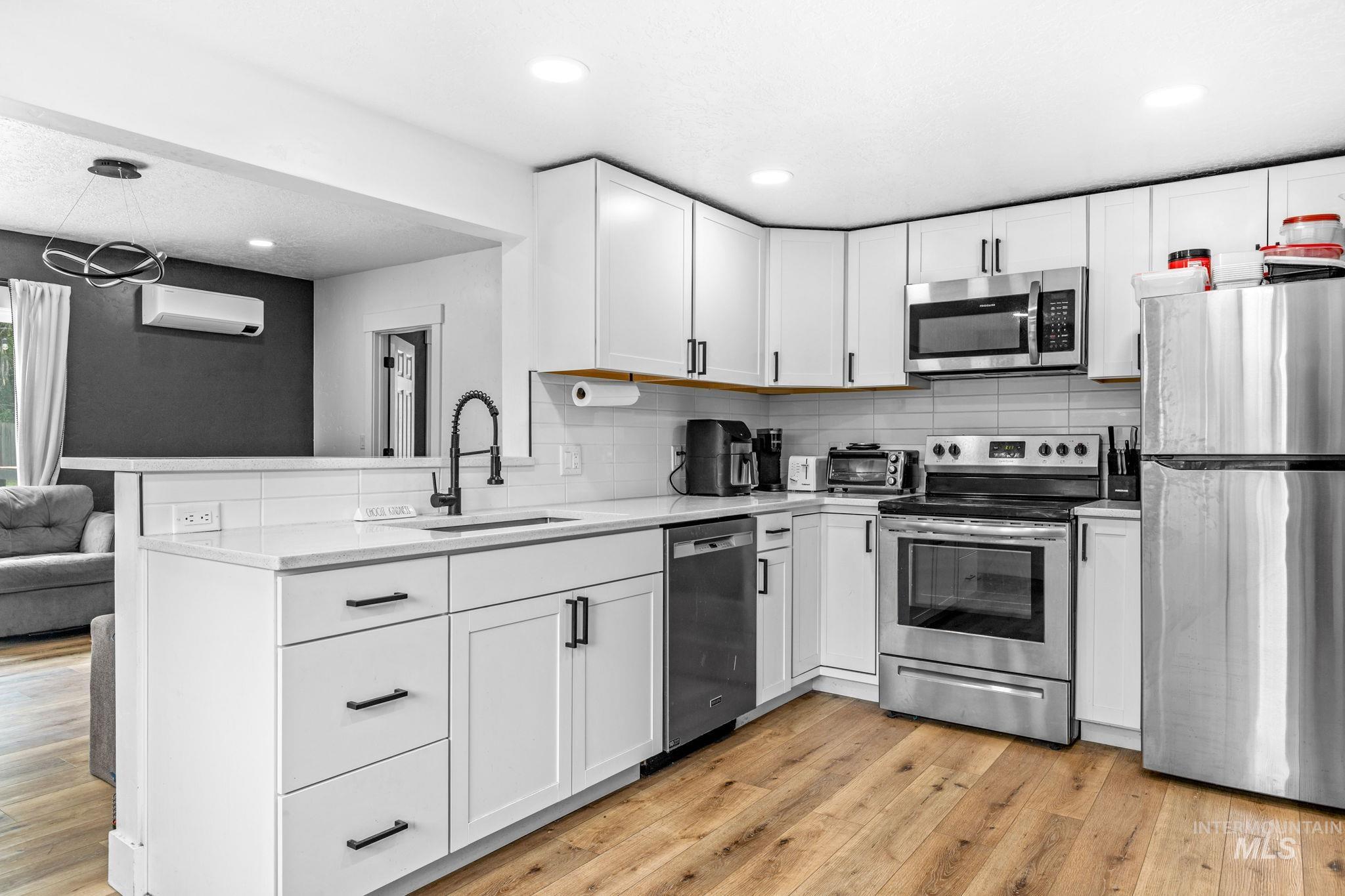 Modern kitchen featuring white cabinetry with black hardware, stainless steel appliances, a white tile backsplash, and wood-finish flooring