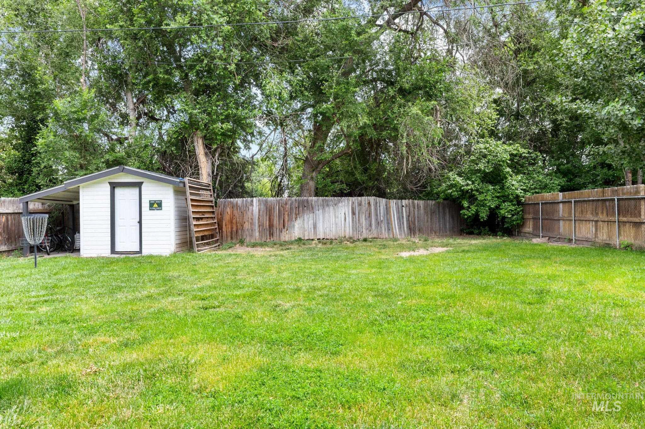 Expansive lawn area featuring a white storage shed with dark trim, a covered side extension, and a wood privacy fence